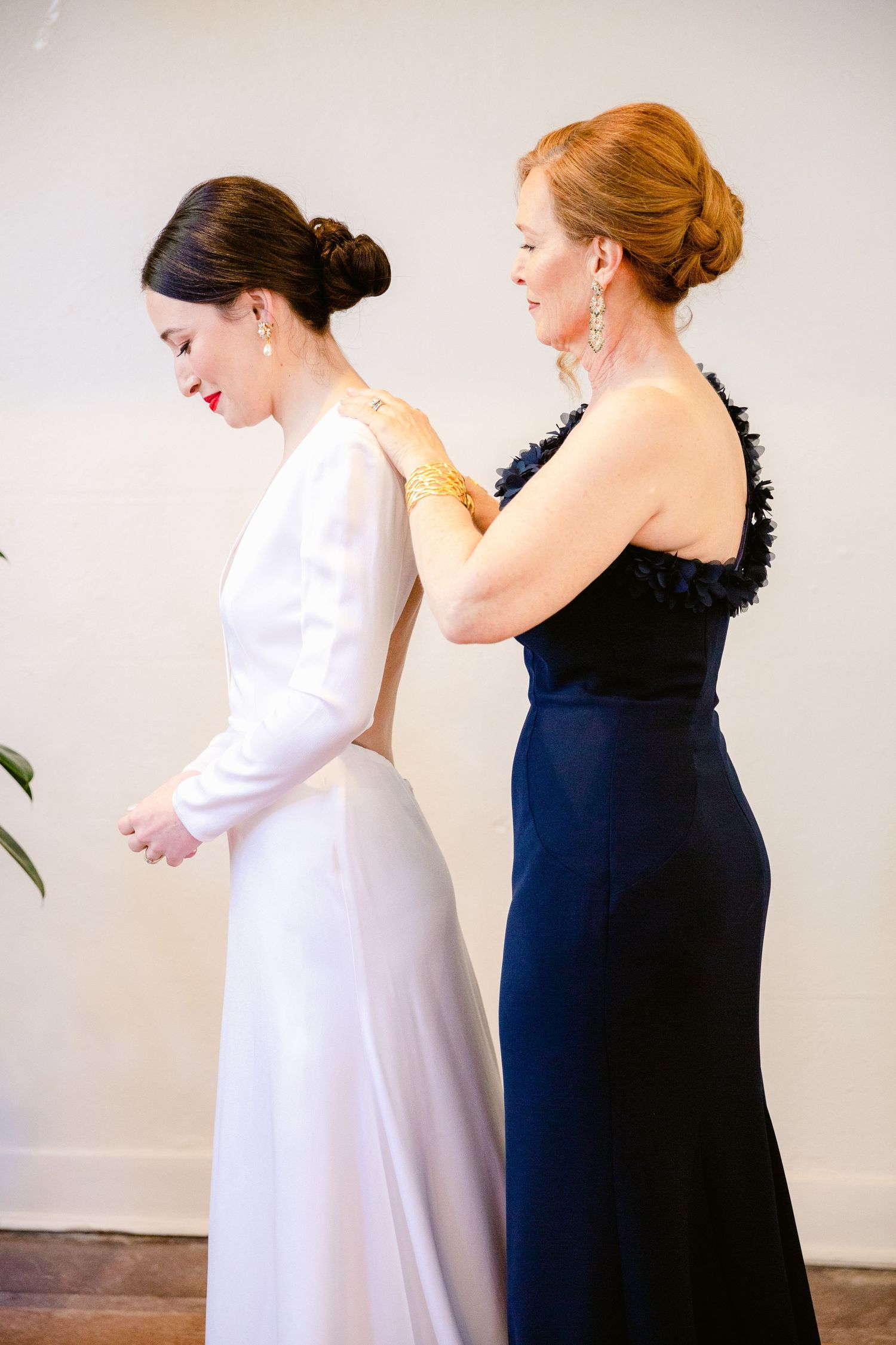 Two people in contrasting white and navy dresses stand together in a candid photo series against a light background.
