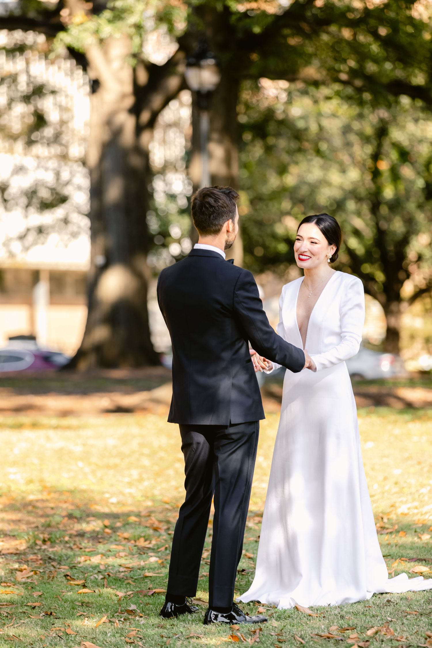 A joyful wedding moment captured in a park with autumn trees in the background.