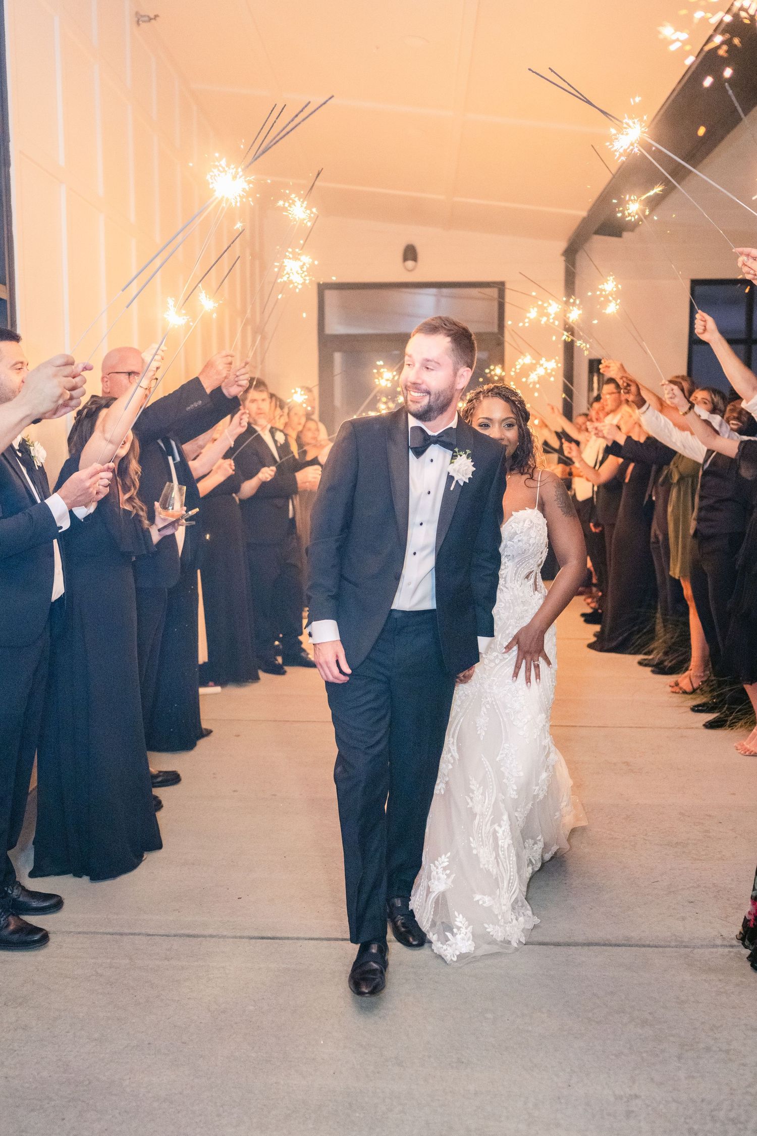 Wedding guests holding sparklers create a magical exit tunnel for the newlyweds at an indoor reception.