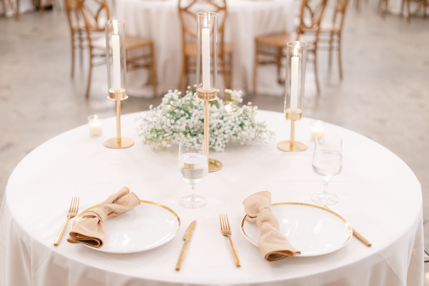 Elegant wedding reception tables set with white linens, gold candlesticks, and delicate baby's breath centerpieces.