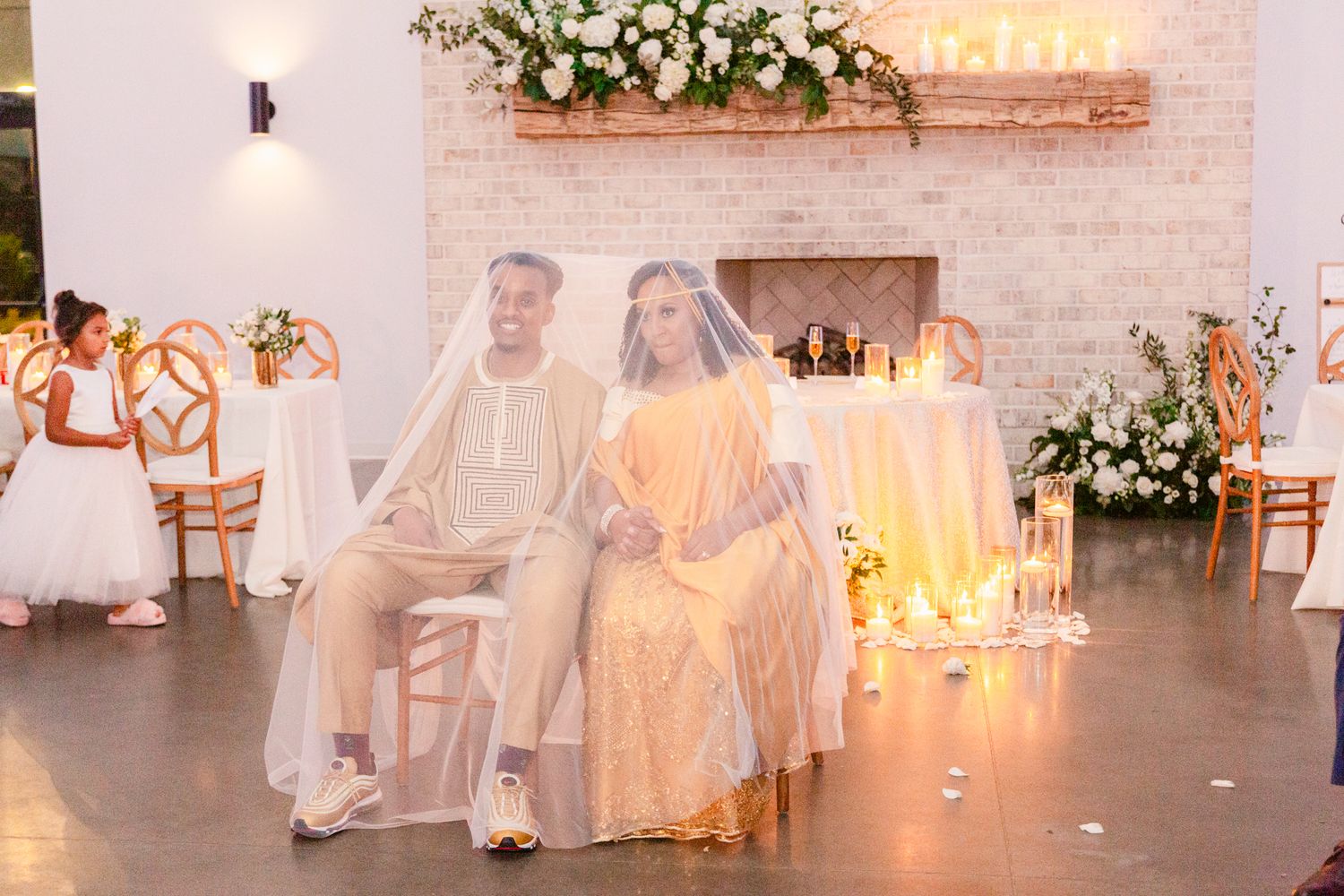 Wedding party dances in a white brick venue decorated with elegant floral arrangements and soft lighting.