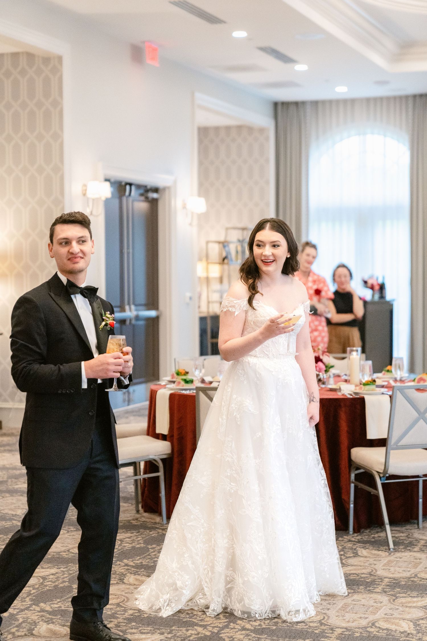 Elegant wedding reception in a bright ballroom with white decor and floral arrangements.