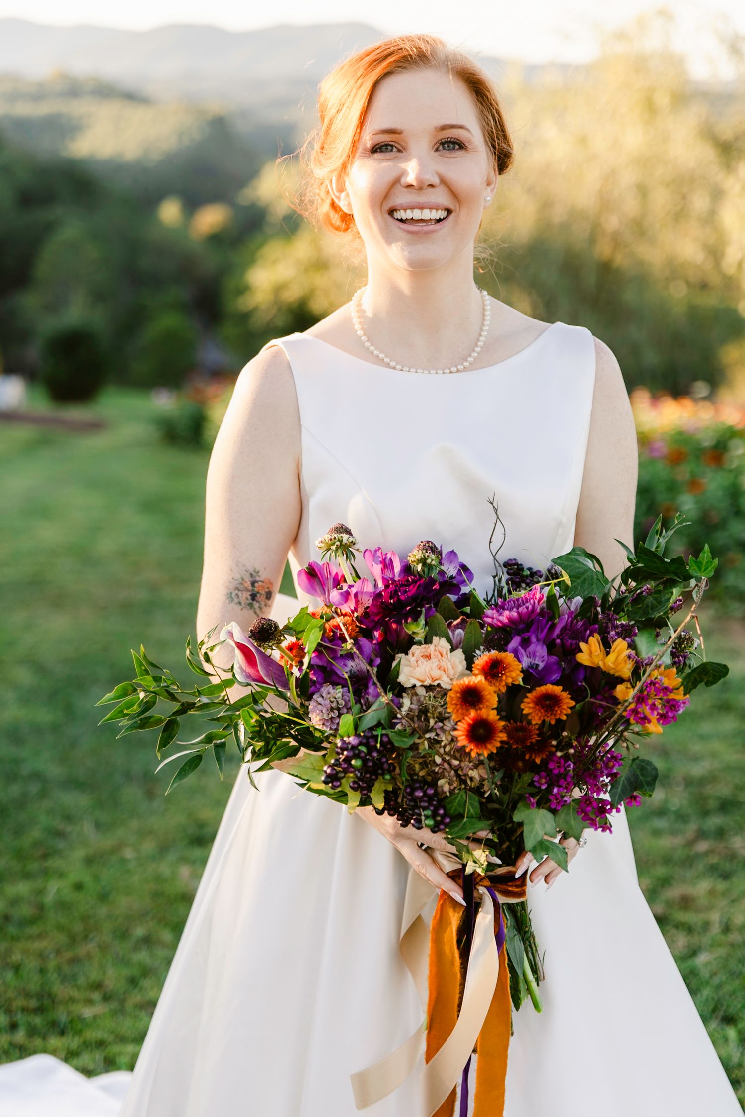Vibrant wildflower wedding bouquet with sunflowers and purple blooms against white dress.