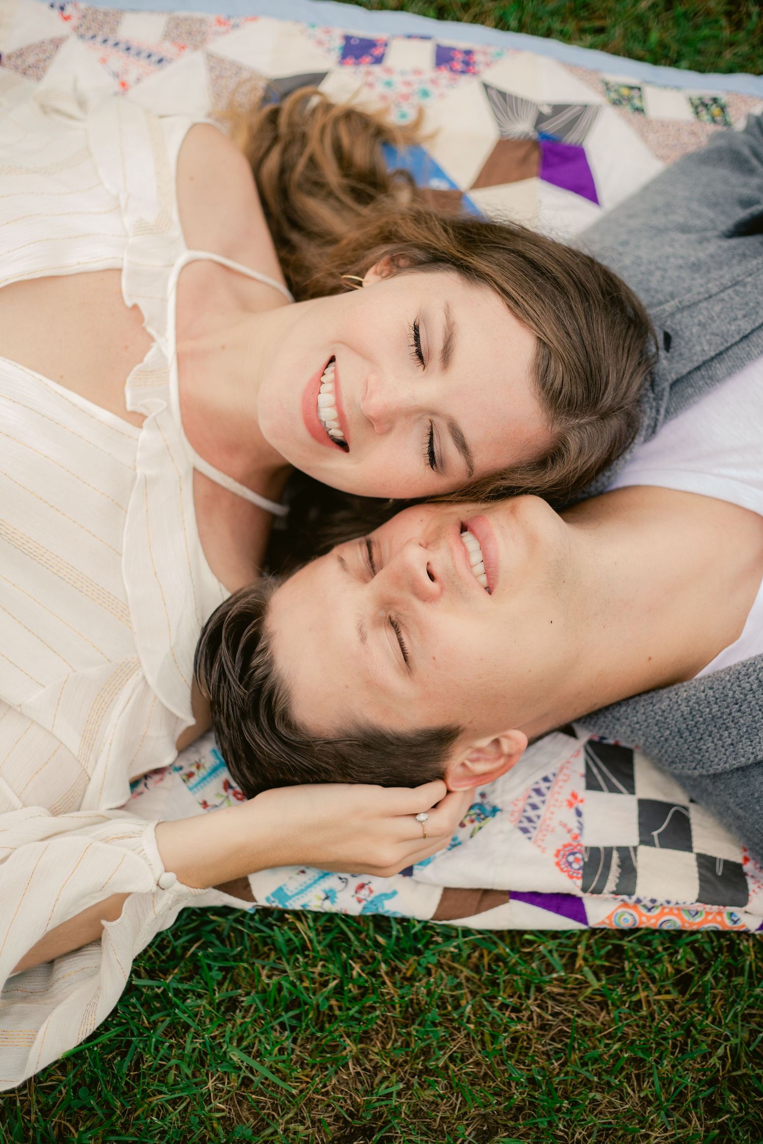 Couple lying on a patterned quilt outdoors expressing joy and intimacy.