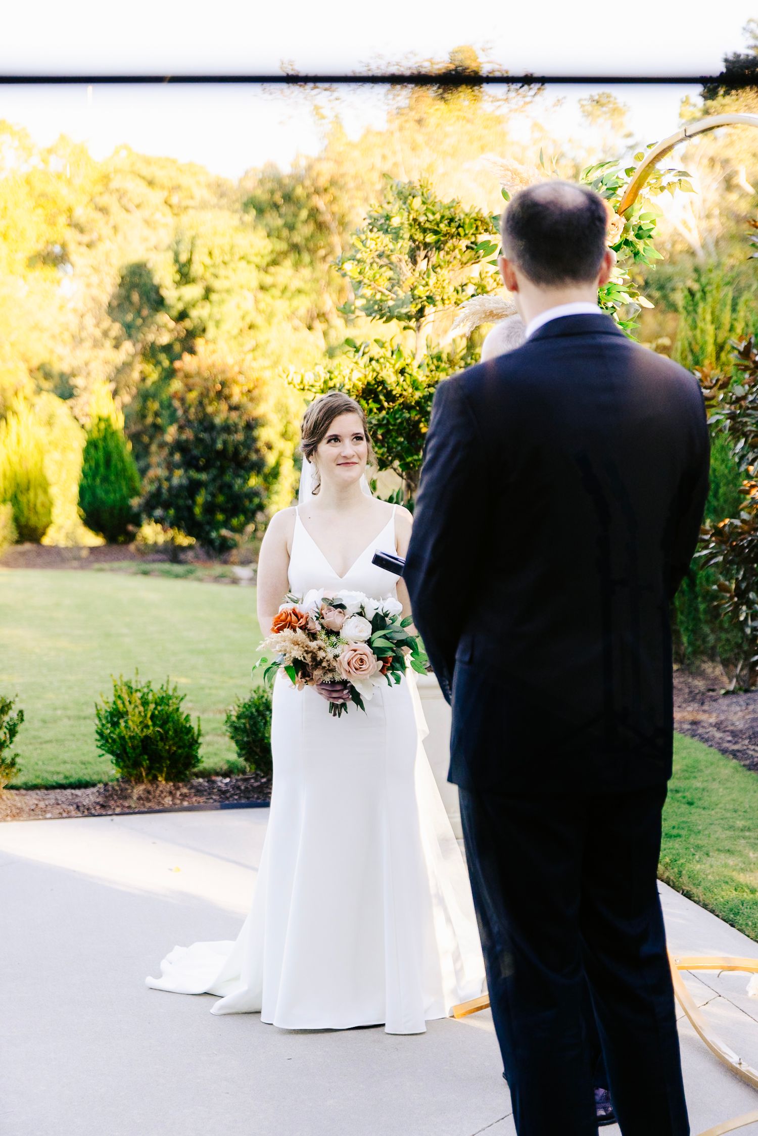 A wedding ceremony moment captured outdoors with lush garden landscaping in the background.
