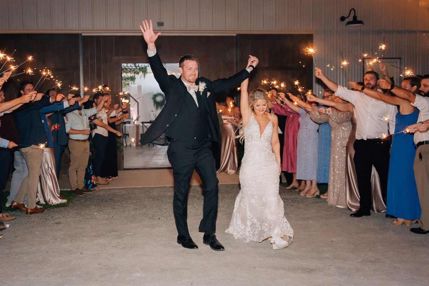 Celebrating newlyweds raise their arms in triumph as guests form a sparkler-lit pathway.