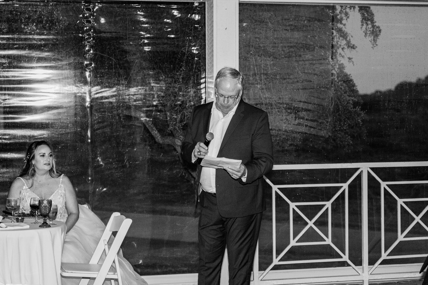 Black and white photo of a wedding reception speech being given on an outdoor patio at dusk.