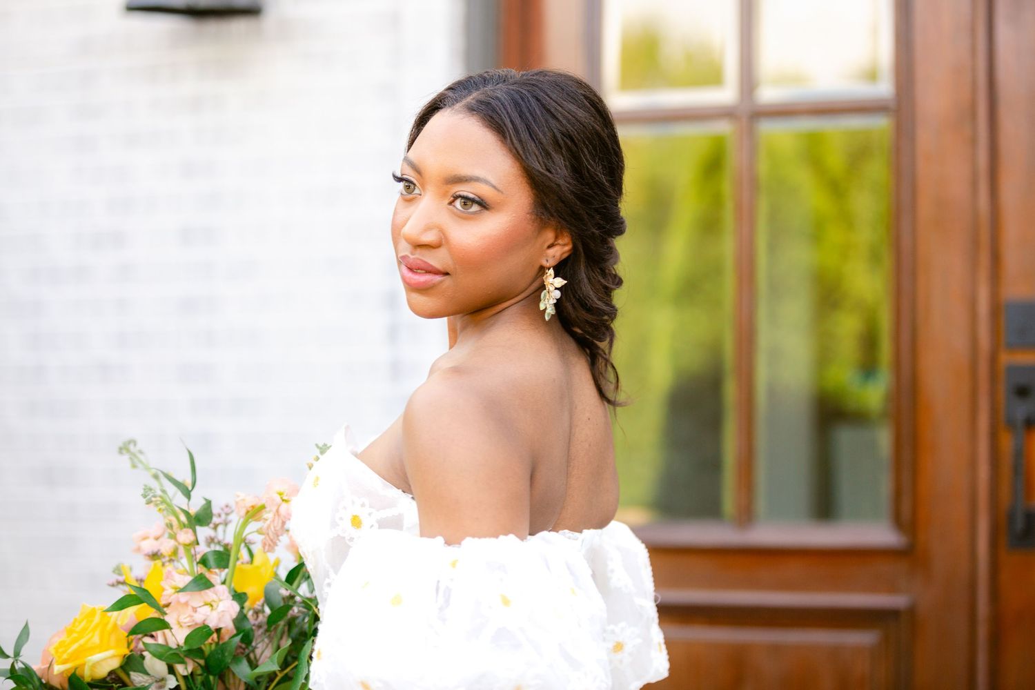A bride in a white wedding dress holds a vibrant yellow and blue floral bouquet during an outdoor celebration.