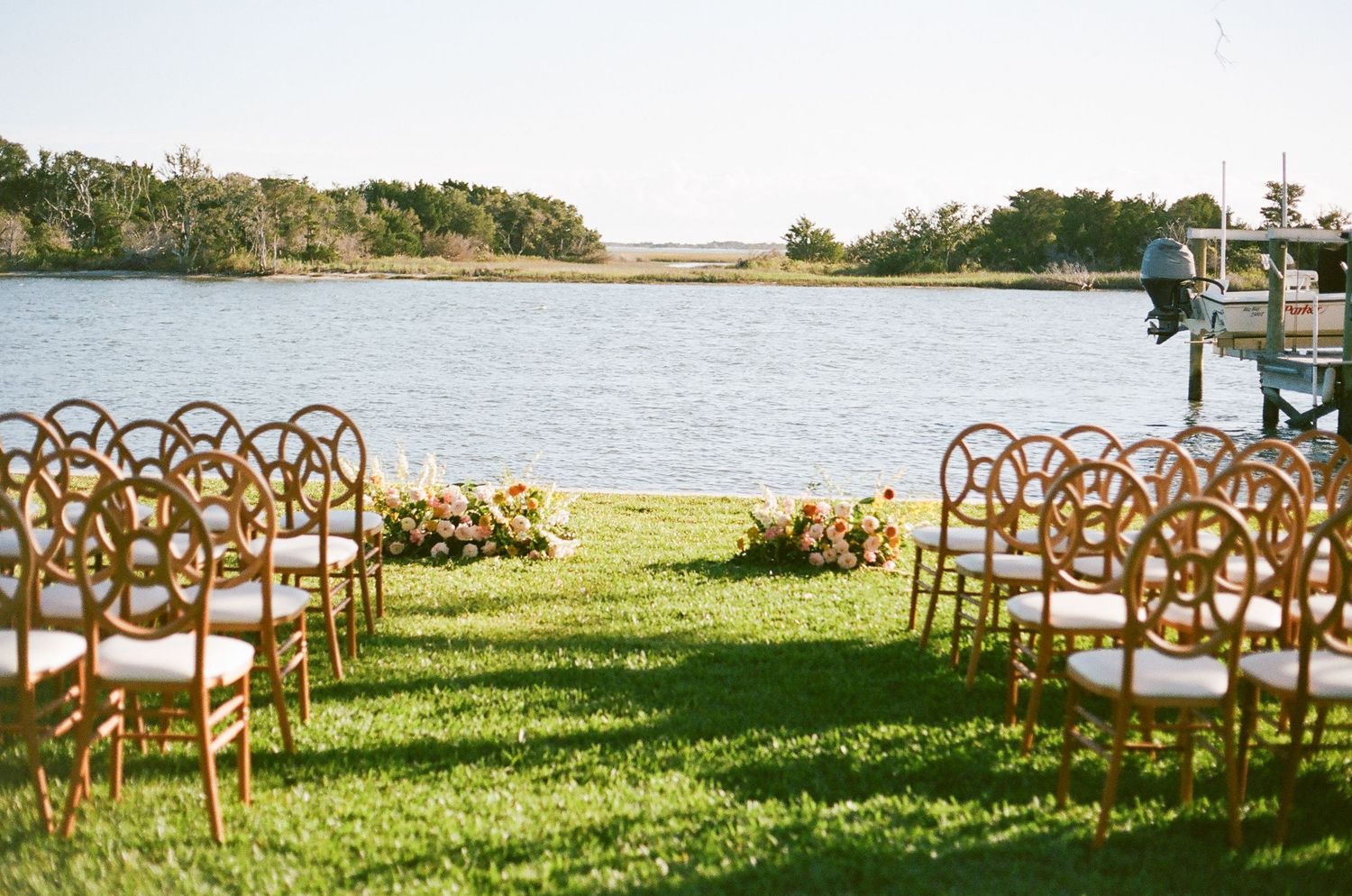 Wooden chairs arranged in rows for an outdoor lakeside wedding ceremony with water views in the background.