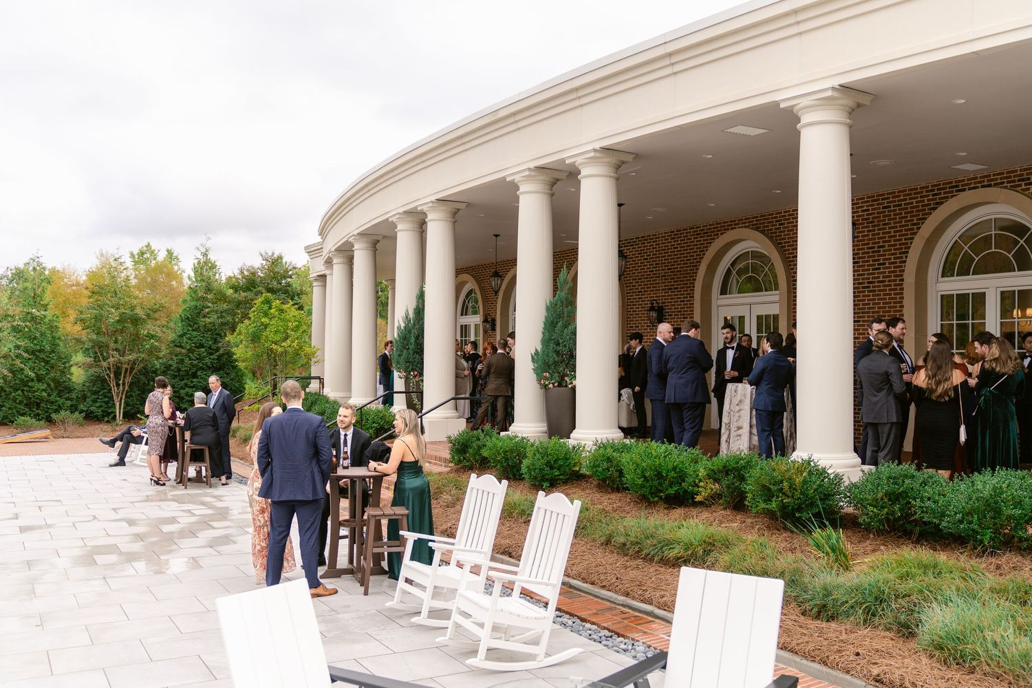 Wedding guests gather on an elegant curved porch with white columns at an upscale venue during an autumn event.