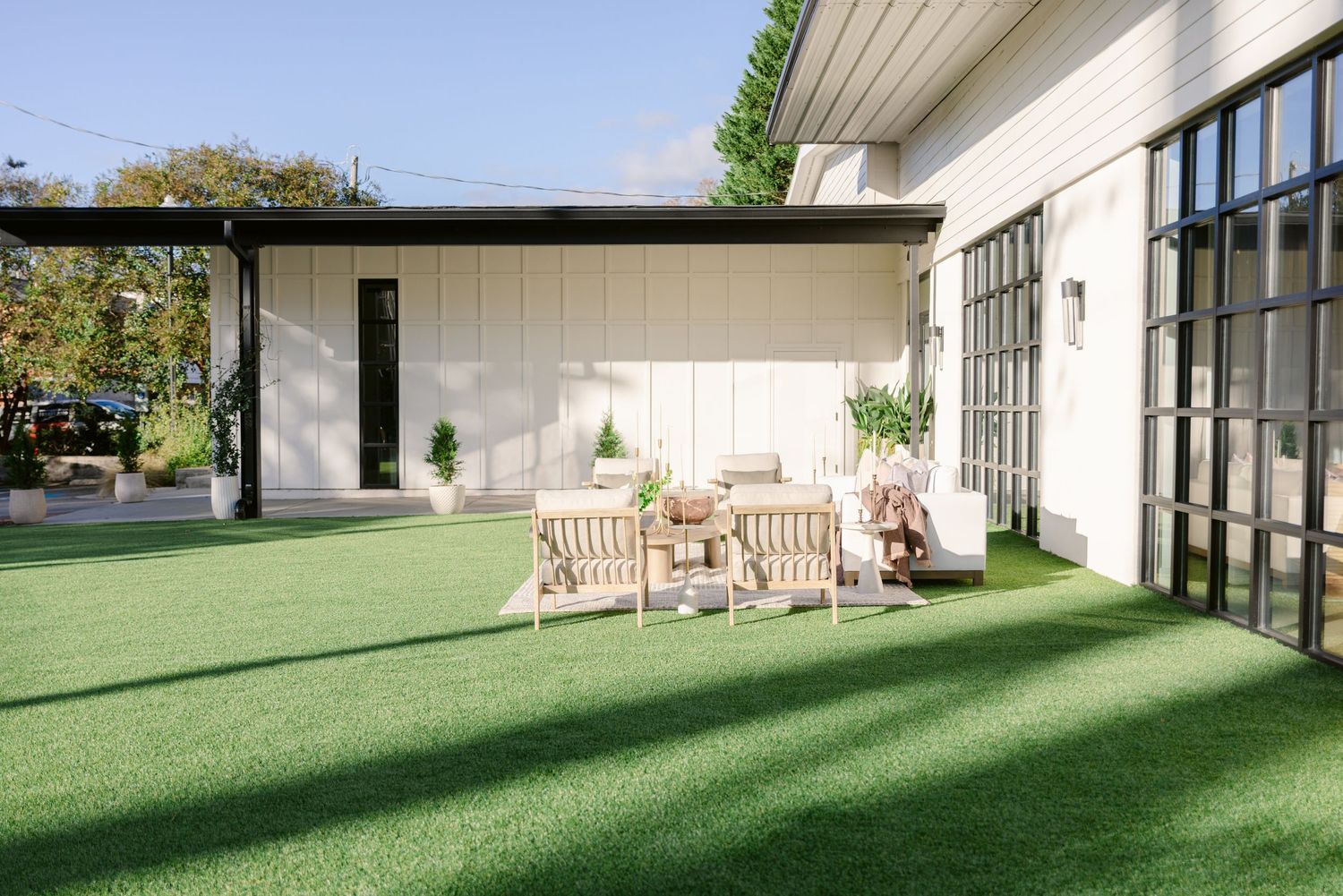 Modern white building exterior with large windows and wooden benches on a manicured green lawn in sunlight.