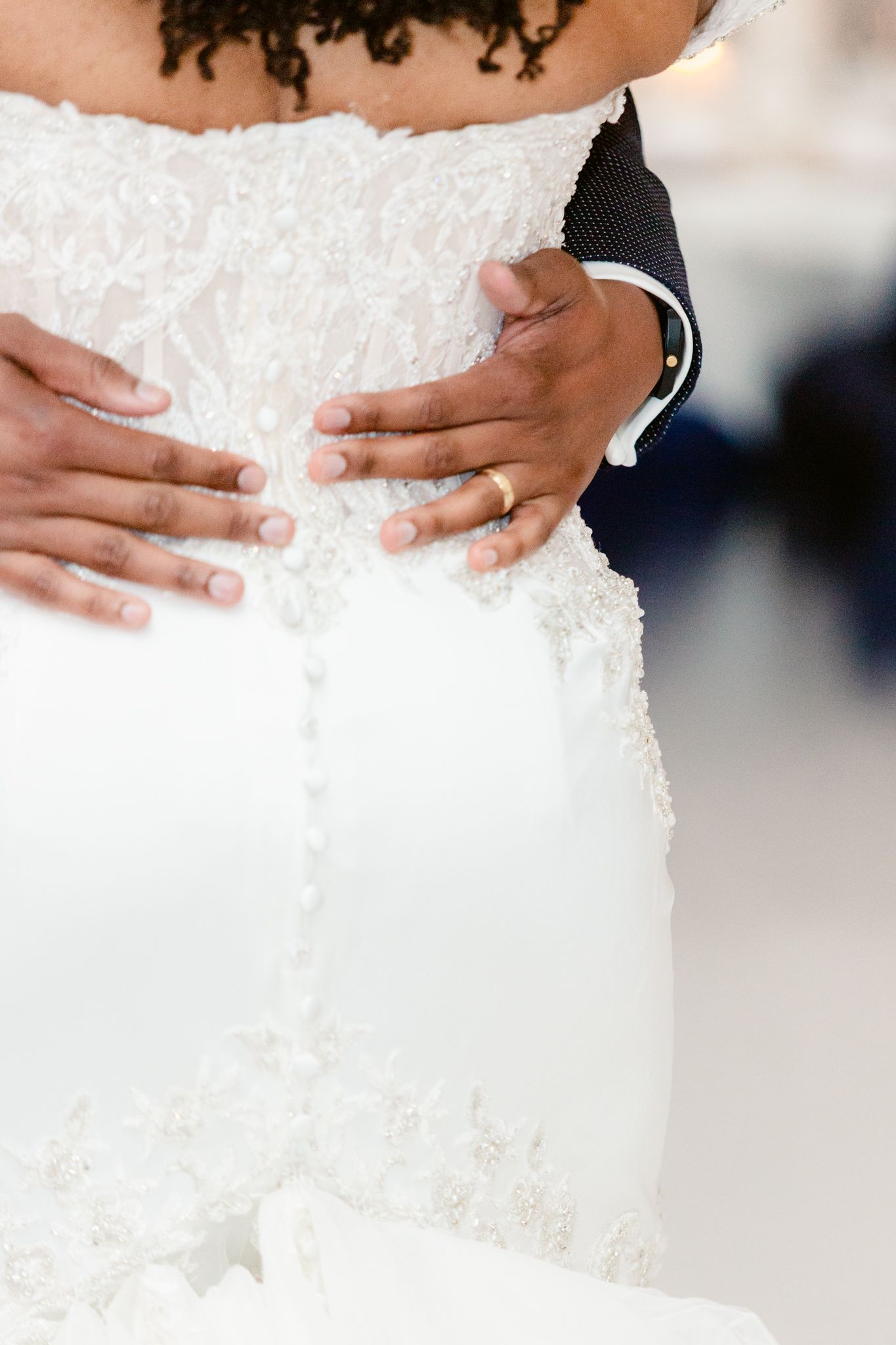 Close-up details of hands touching the intricate lace and beading on a white wedding dress.