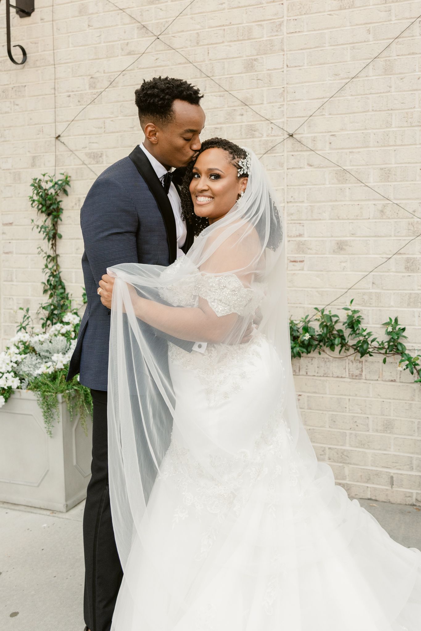 An elegant wedding portrait against a white brick wall with decorative climbing vines.