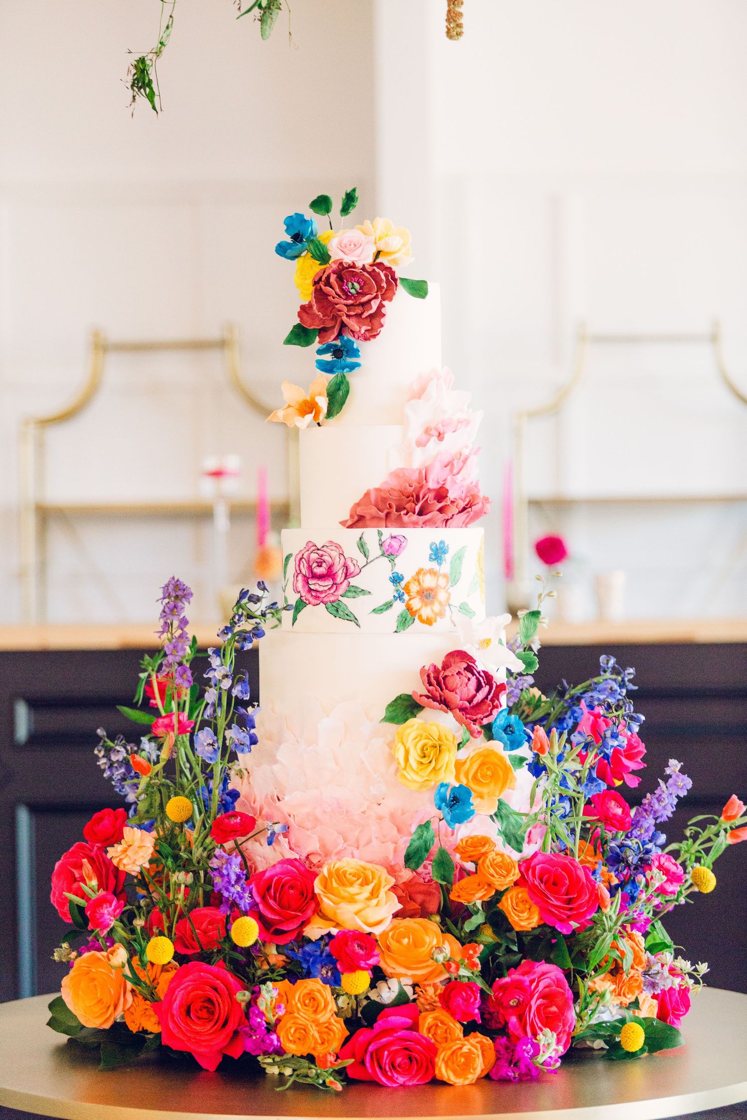 Vibrant multi-colored floral arrangement featuring roses and wildflowers decorates a wedding cake.