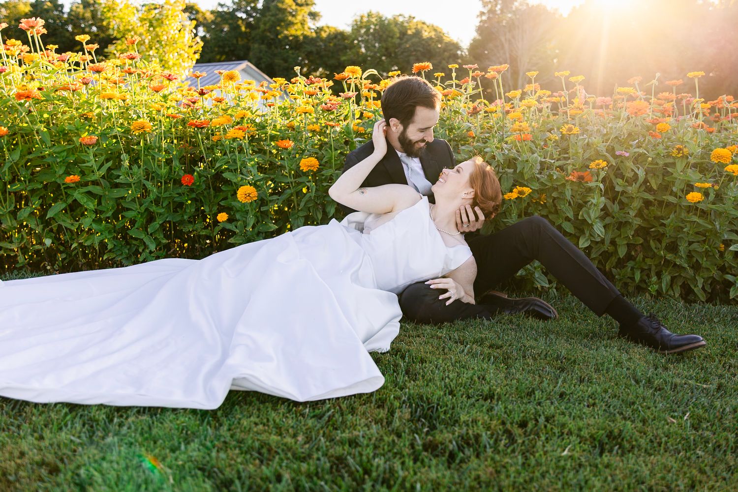 A figure in white dress lies gracefully on grass surrounded by vibrant yellow flowers at golden hour.