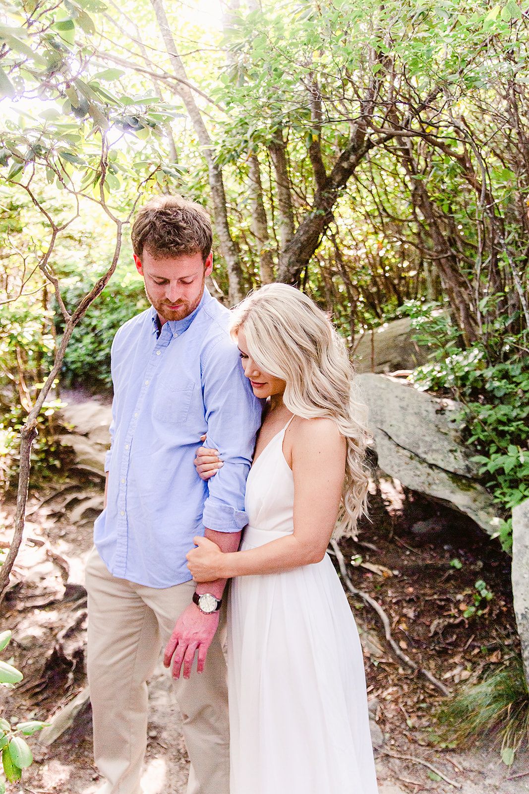 Couple shares an intimate moment on a wooded path surrounded by lush greenery and rocks.