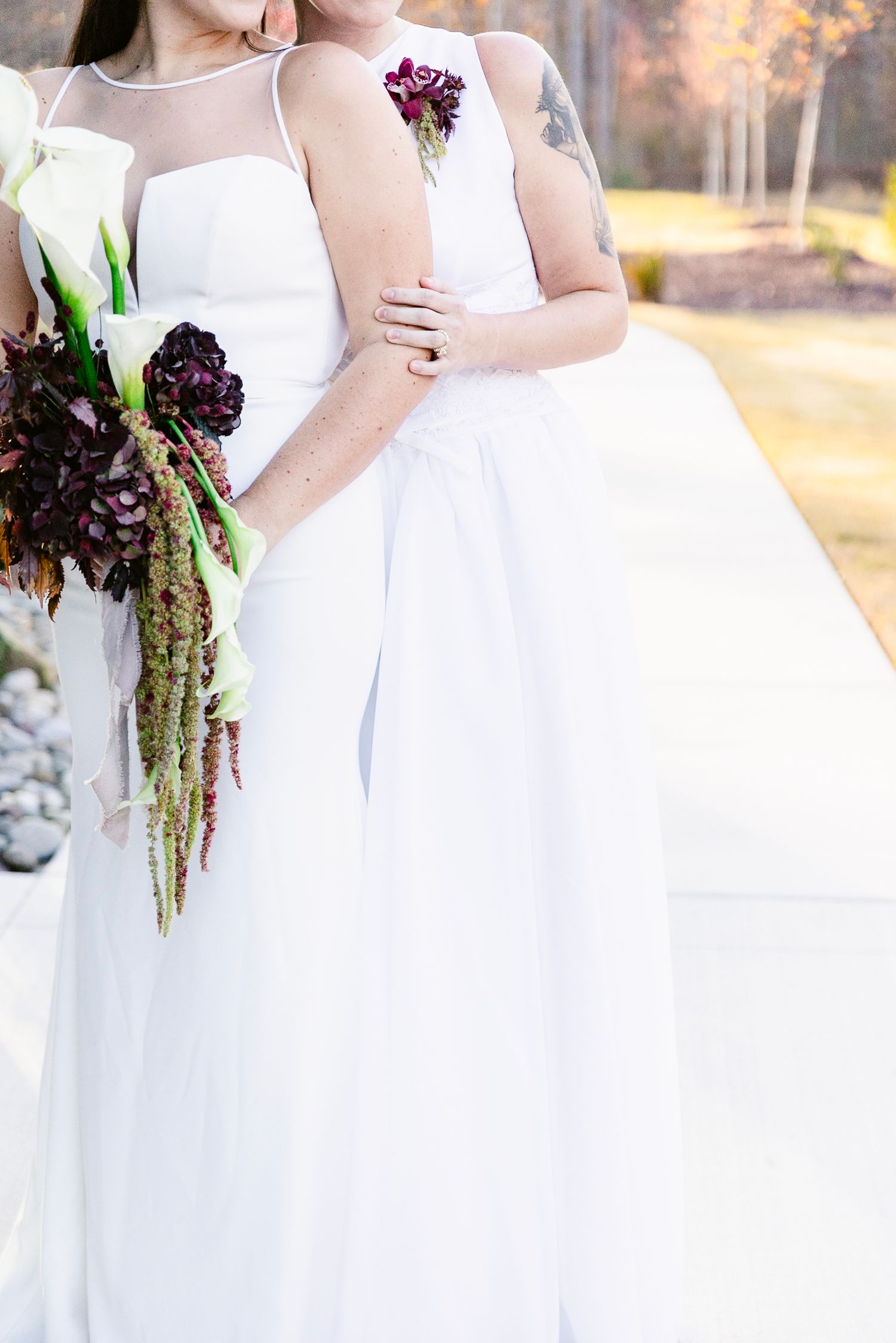 A row of bridesmaids in white dresses hold deep purple and burgundy floral bouquets at an outdoor wedding ceremony.