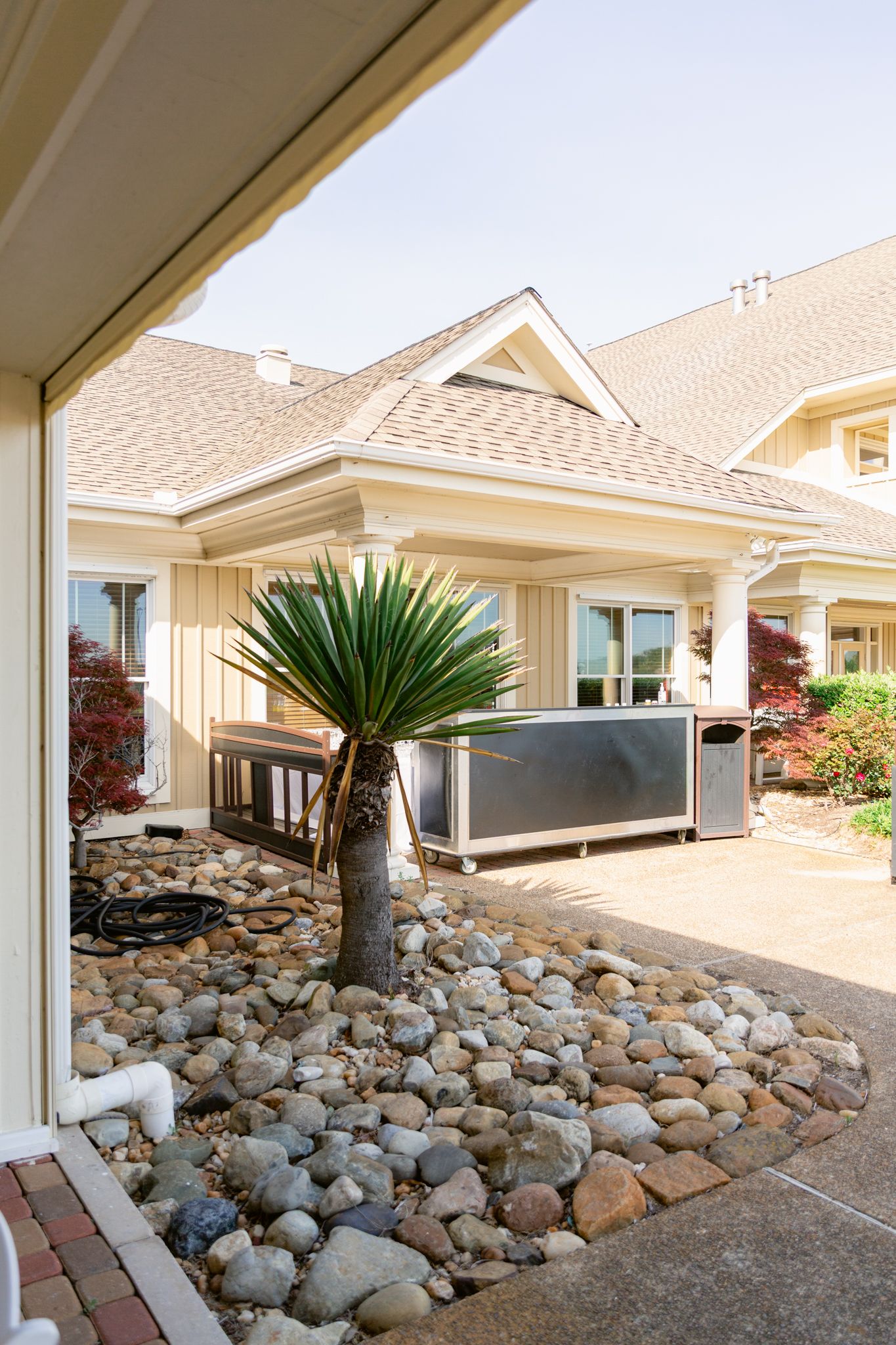 Modern beige house exterior with desert landscaping featuring large rocks and a palm tree in the front yard.