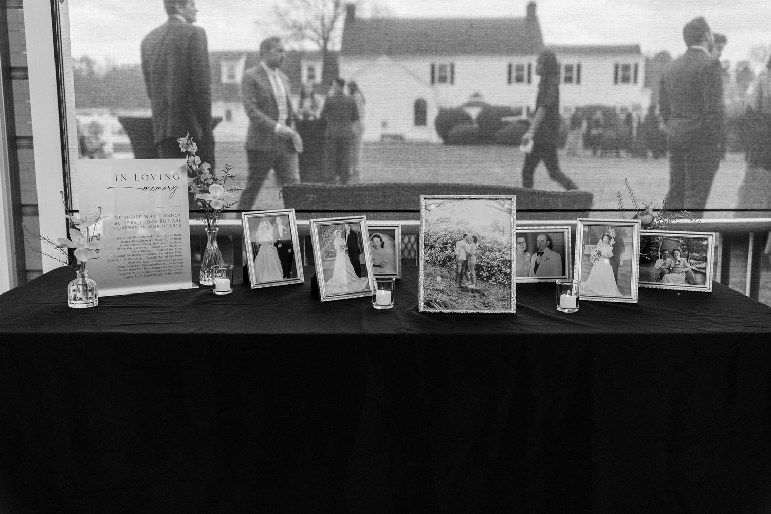 Black and white photograph showing vintage family photos displayed in frames on a dark table surface.
