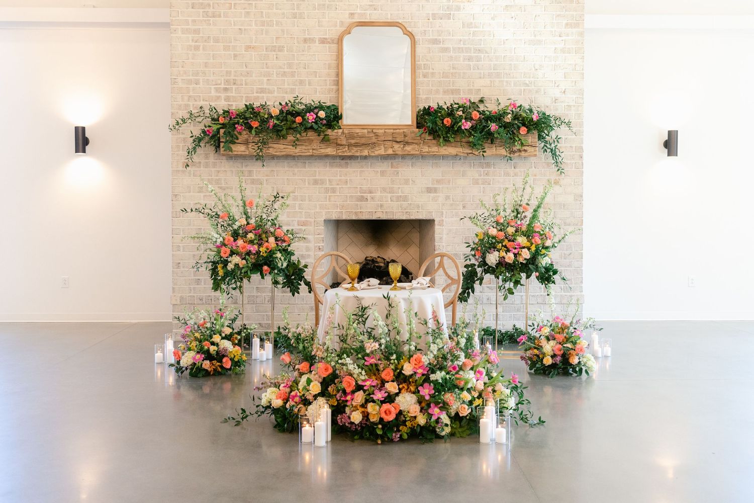 Elegant wedding reception venue decorated with lush floral arrangements and white candles on stone fireplace mantel.