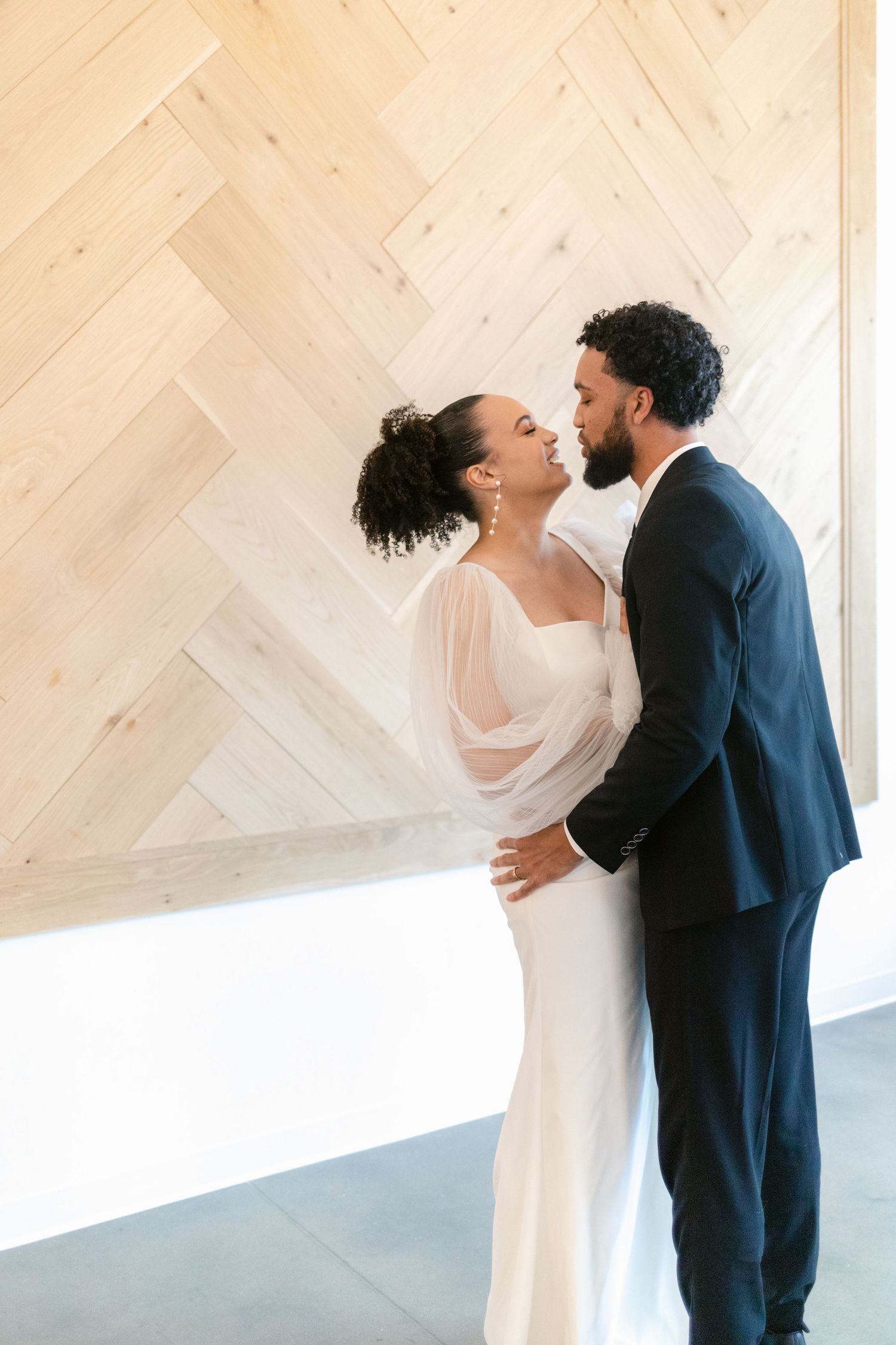 A series of four romantic wedding photos showing a couple in white dress and navy suit embracing against a light wooden wall.