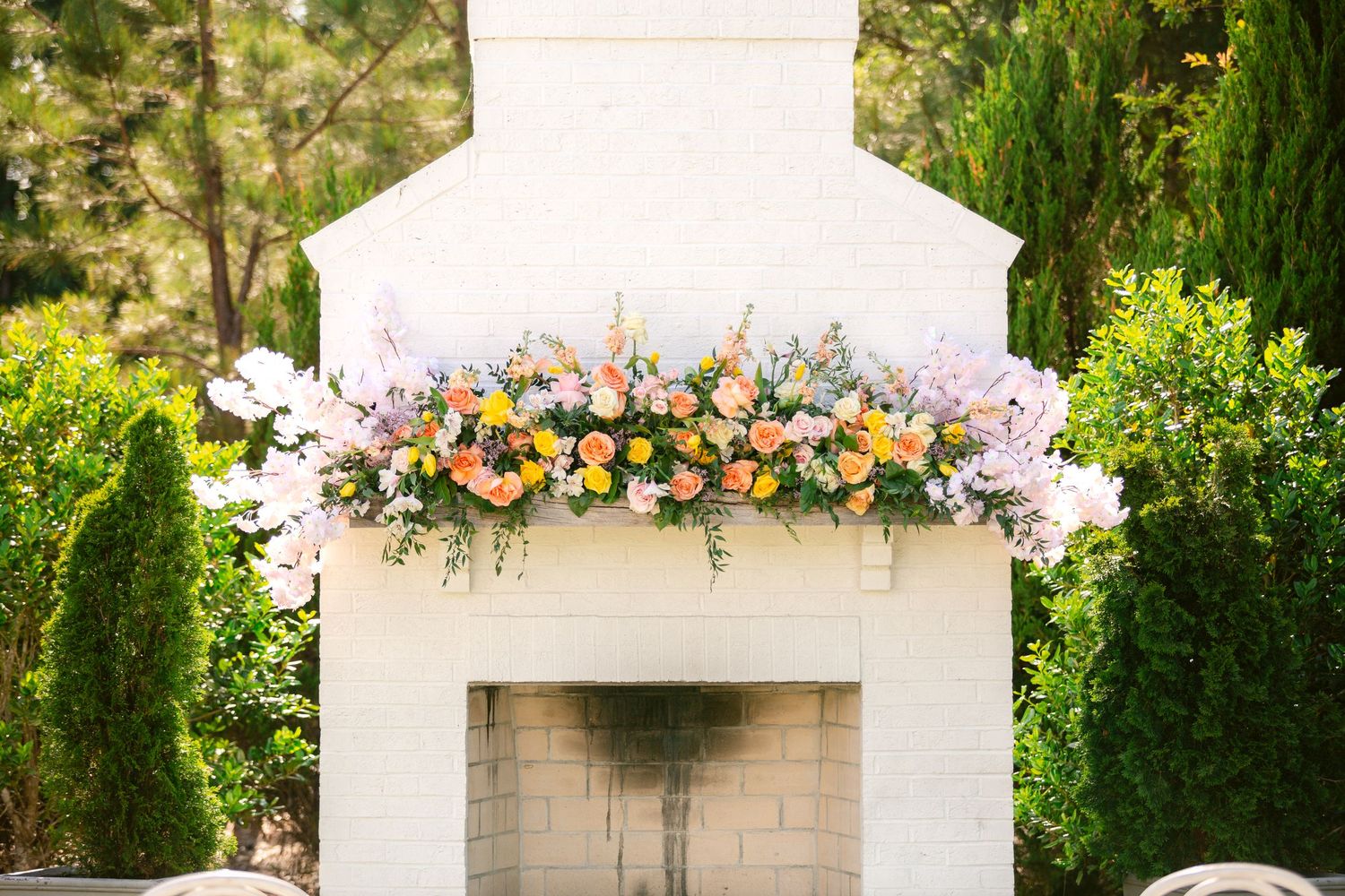 A white outdoor wedding gazebo decorated with colorful floral arrangements and greenery in a garden setting.