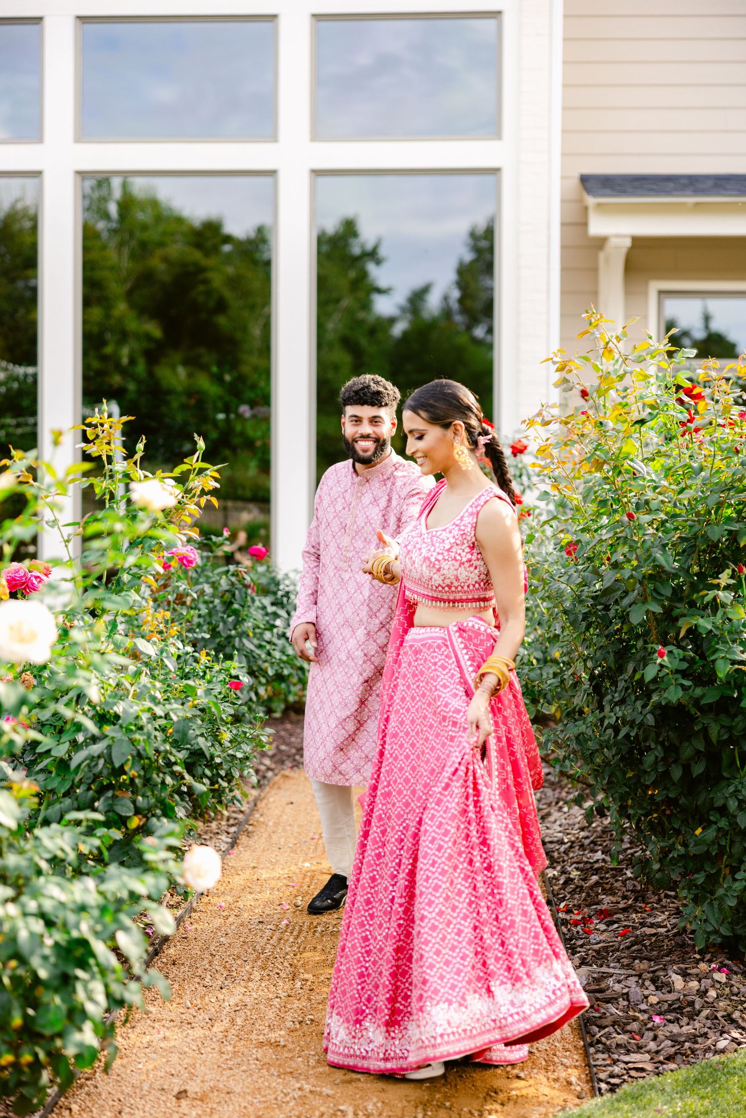 A couple shares a romantic moment in a garden path lined with blooming pink and yellow flowers.