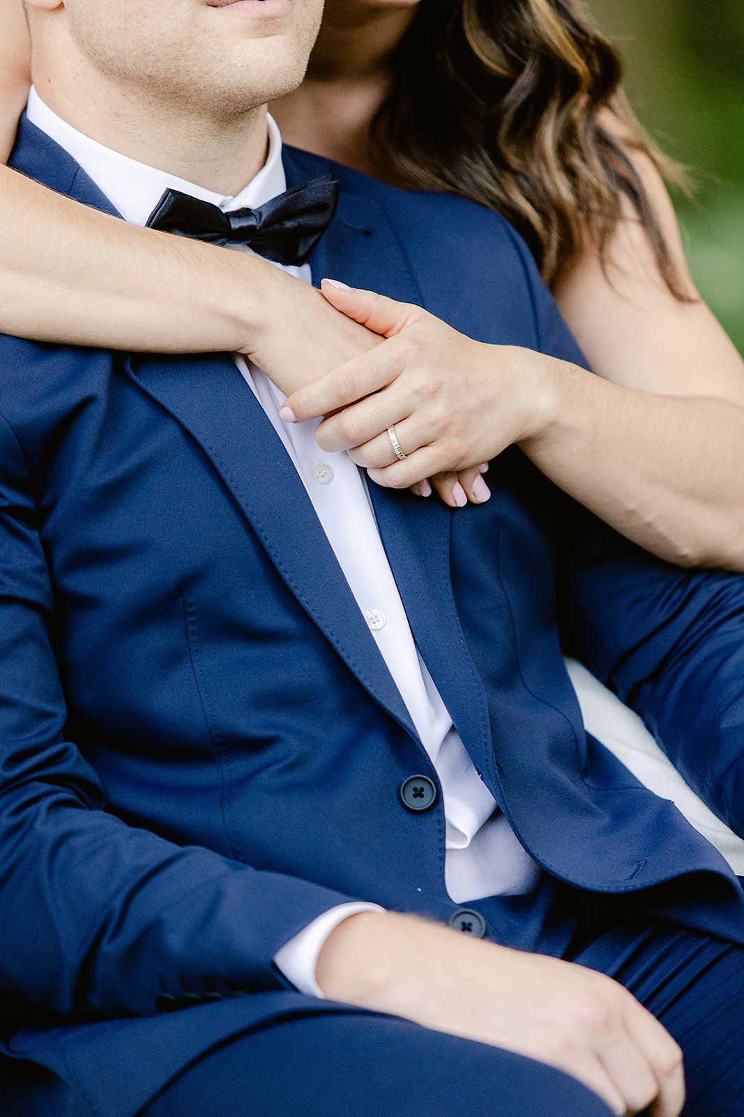 Close-up of hands resting on a navy blue suit sleeve showing wedding rings and elegant watch details.