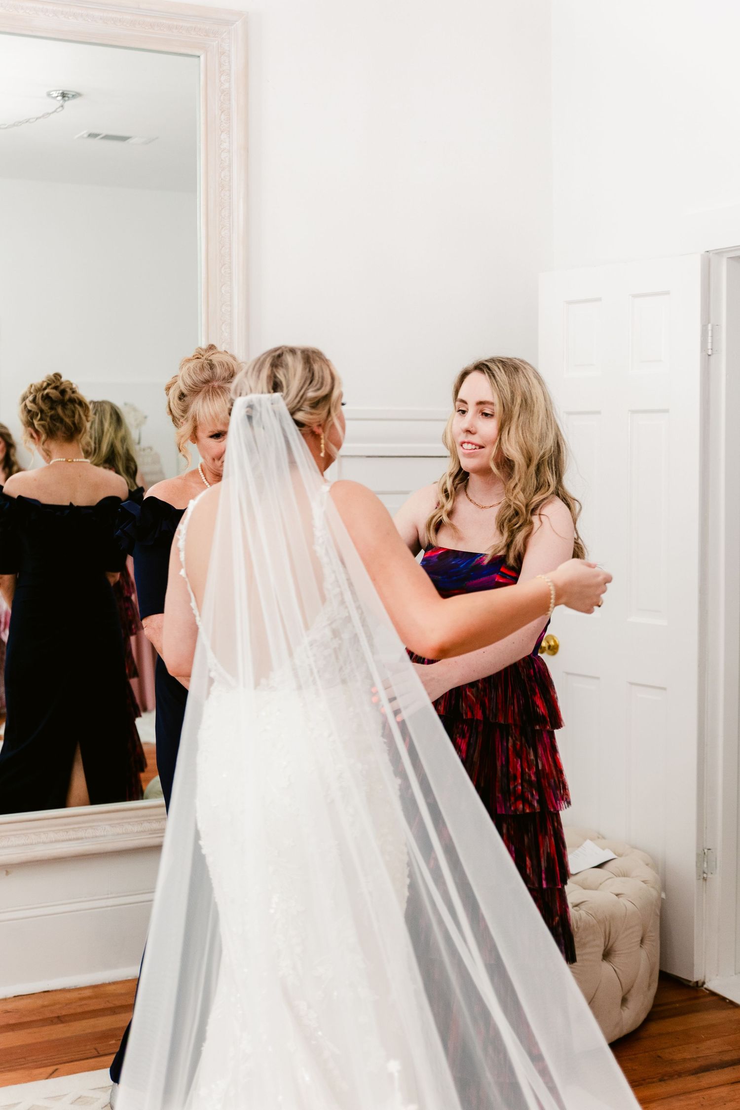 A bride in a flowing veil shares emotional moments with wedding party members in a bridal suite.