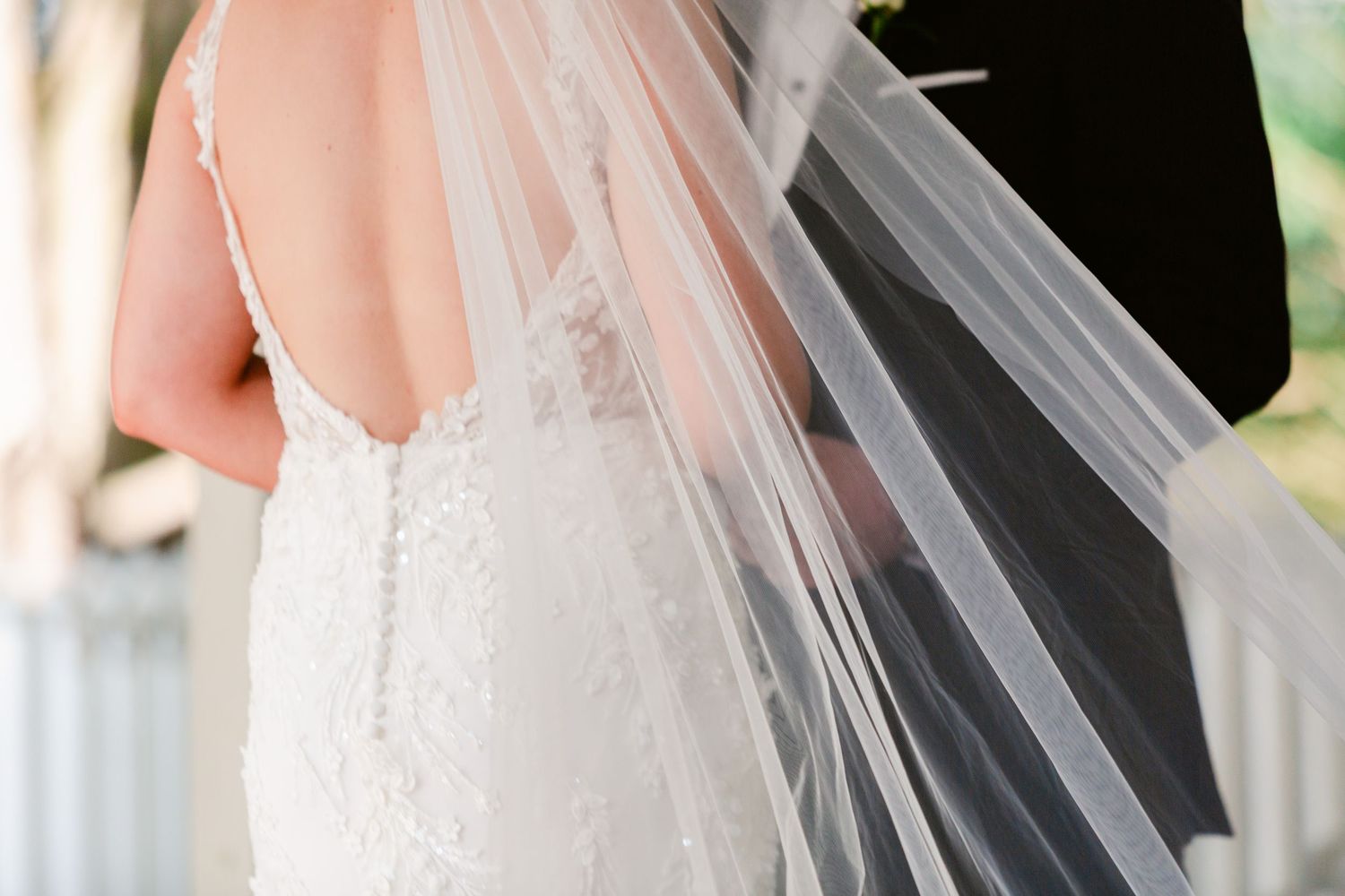 An elegant white wedding veil with delicate lace detailing flows in a gentle breeze against a light background.
