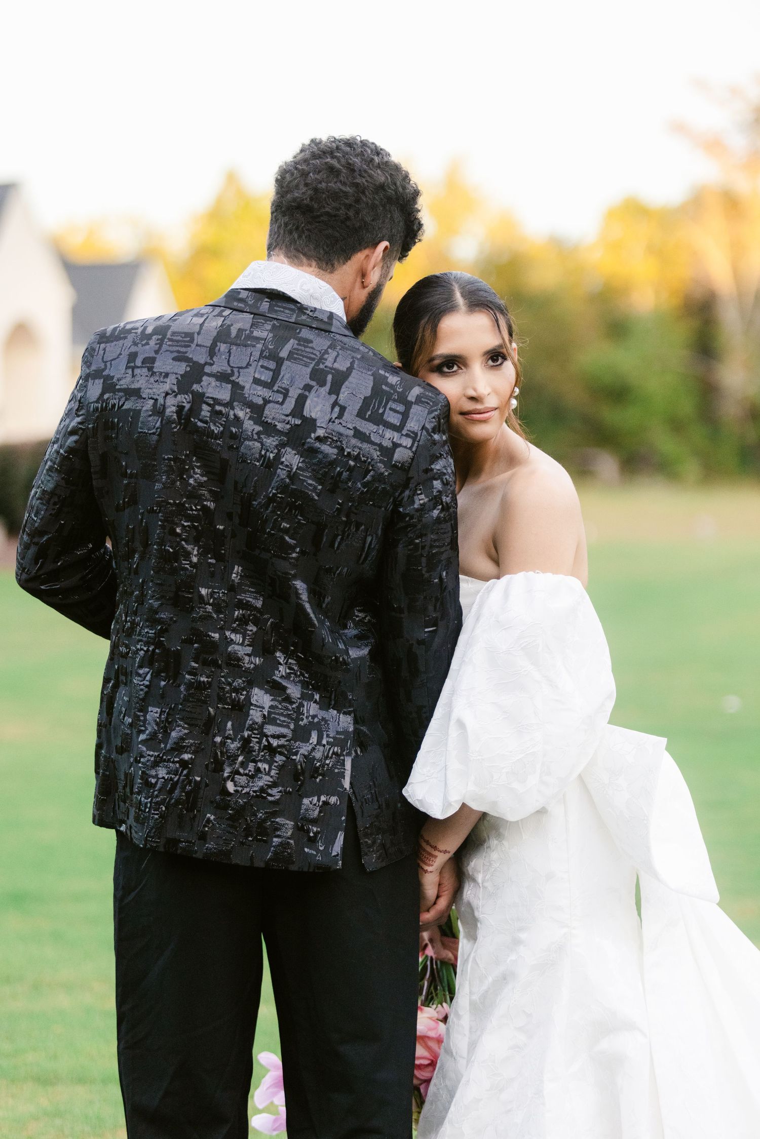 Stylish couple in black and white outfits pose together in an outdoor garden setting during golden hour.