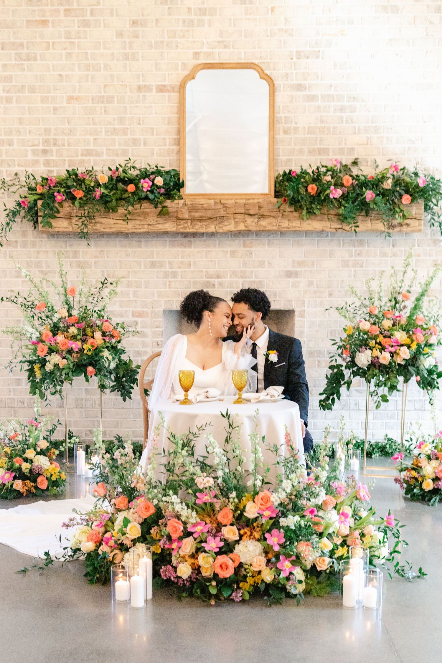 Romantic wedding reception setup with coral and pink floral arrangements against exposed brick walls in modern venue.