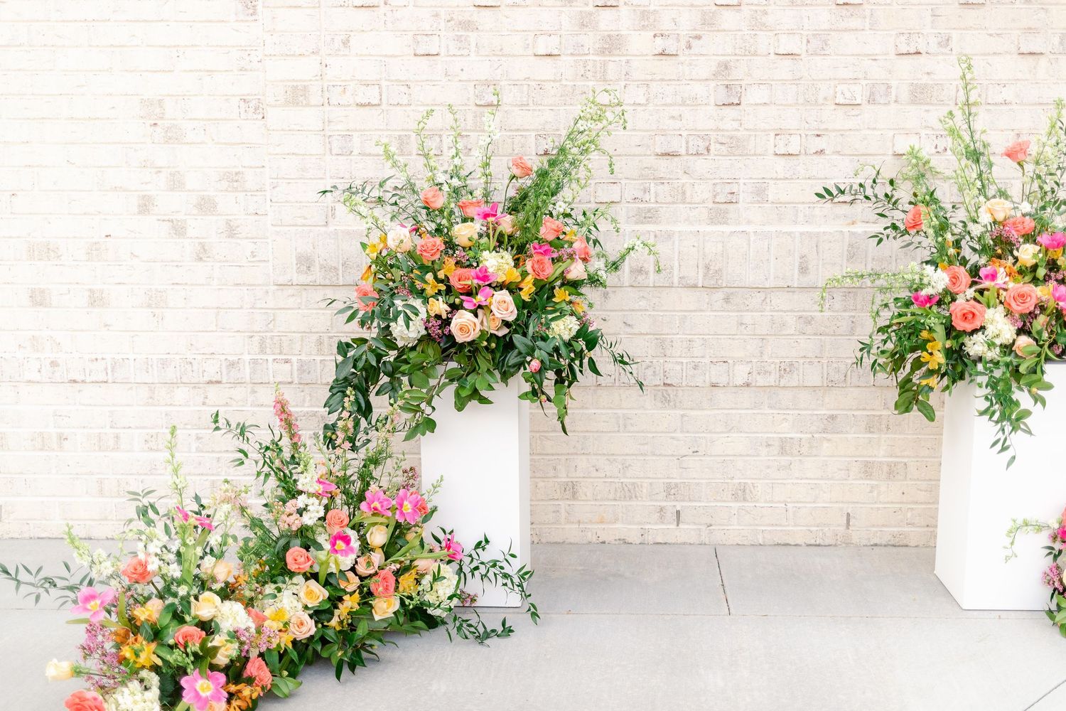 Elegant floral arrangements with pink and peach blooms decorate a light brick wall at a wedding venue.