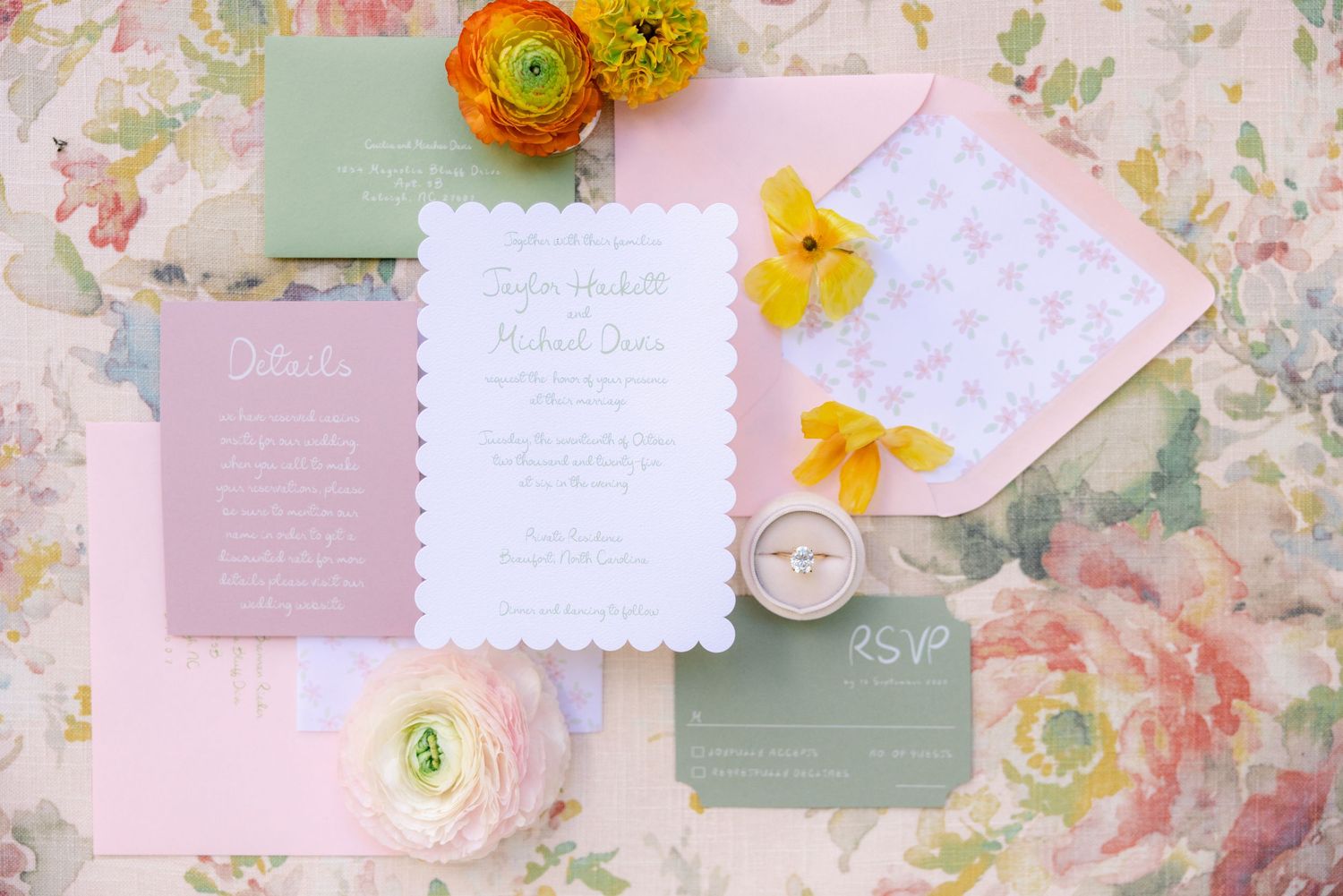 Wedding invitation suite with pink and green cards decorated with yellow and orange ranunculus flowers on floral background.
