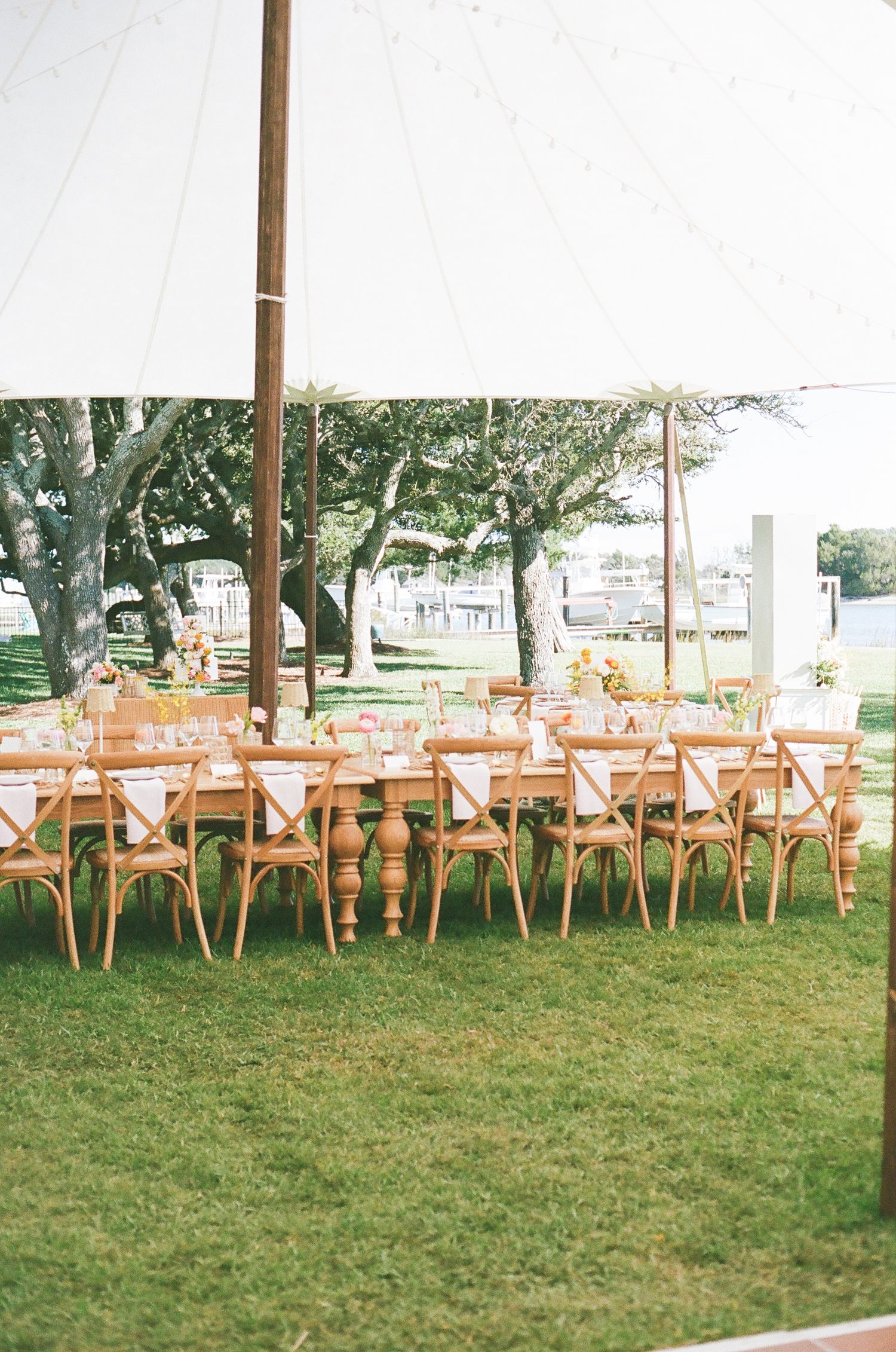 Outdoor wedding reception setup with wooden crossback chairs under white tent canopy.