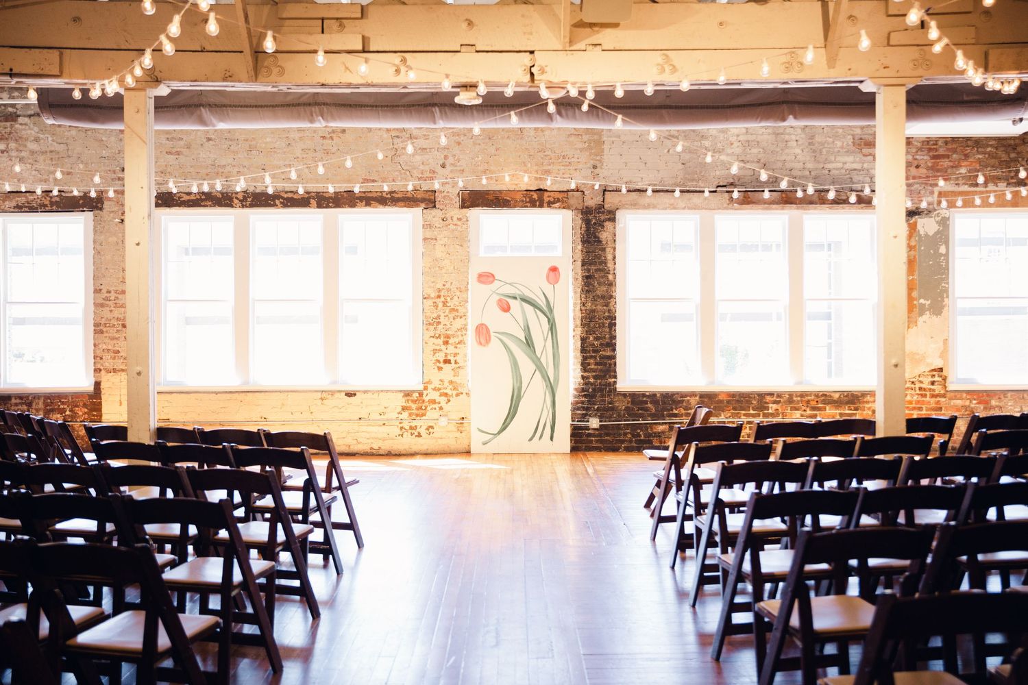 Wedding ceremony space with rows of black chairs and string lights in an industrial-style venue.