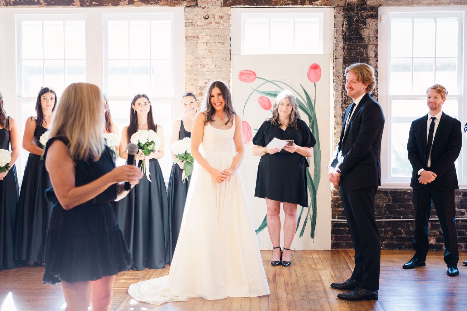 A wedding ceremony in progress with attendants in navy dresses and decorative floral artwork.