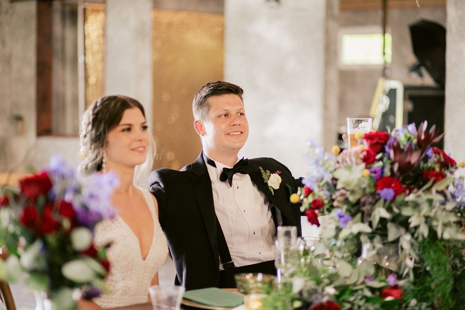 A couple seated at their reception table with vibrant floral arrangements.