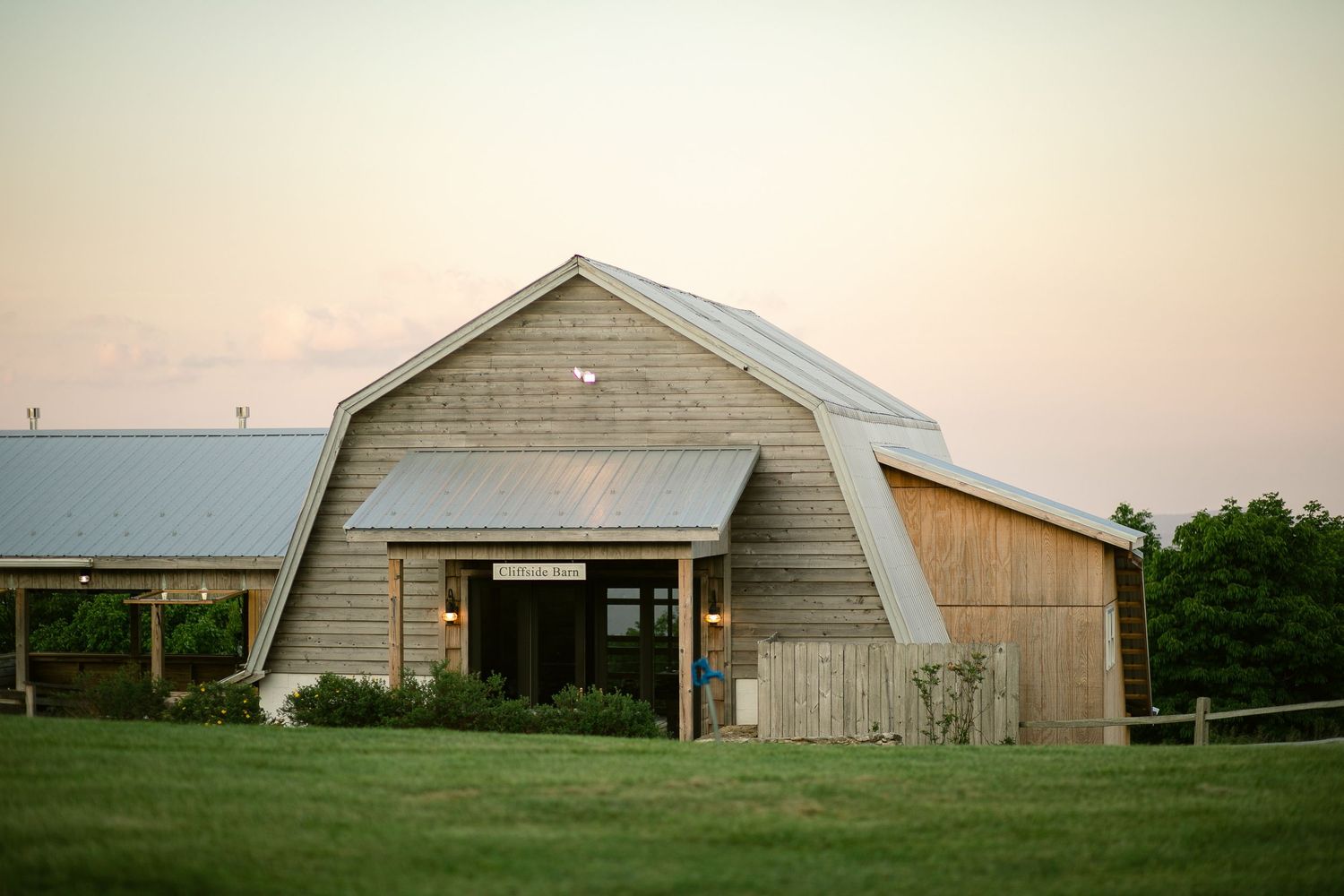 Large rustic barn venue with curved roof at sunset in countryside setting.