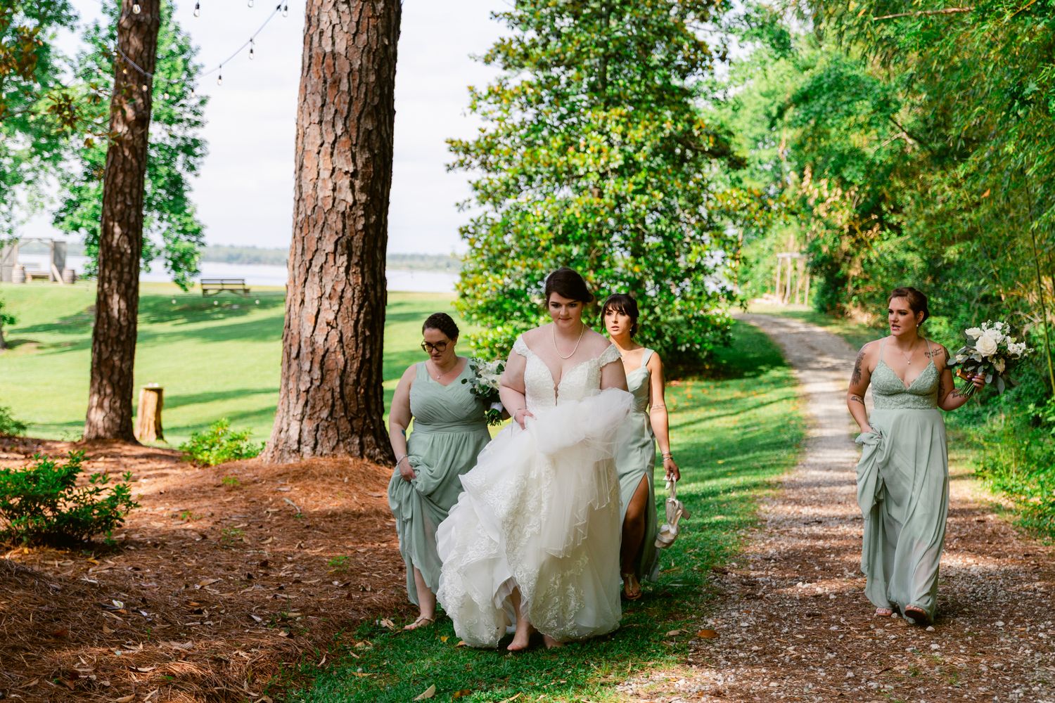 A group walks along a tree-lined path in formal attire during a summer wedding celebration.