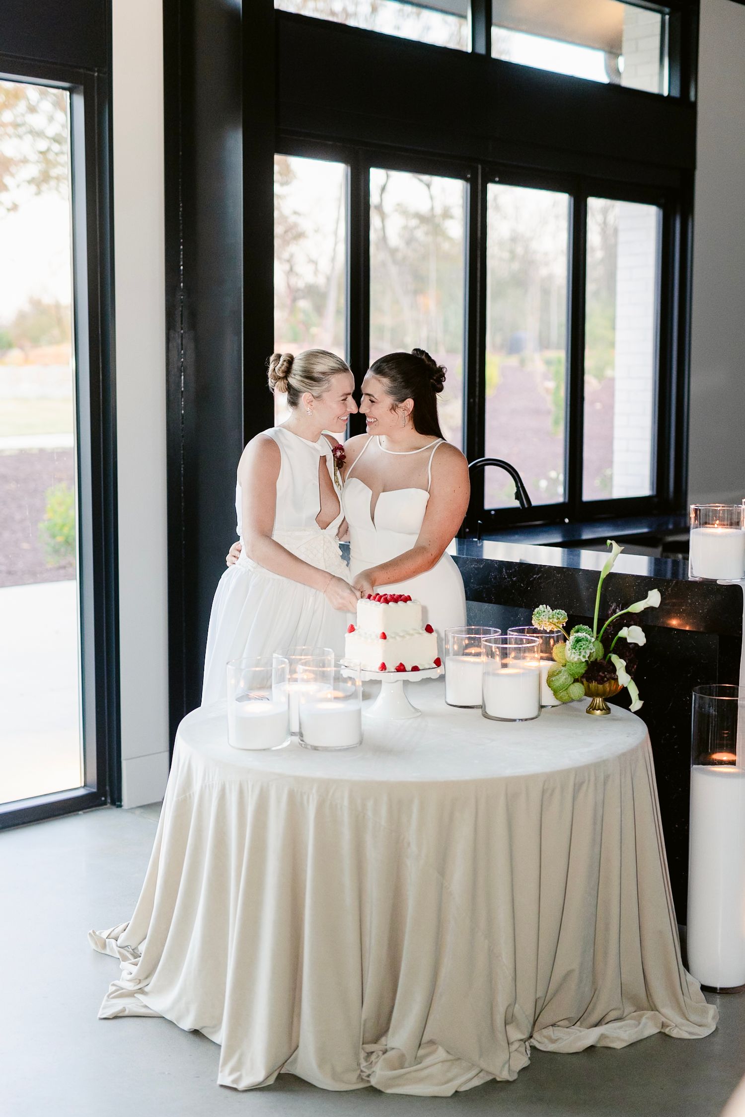 A romantic wedding reception scene with a couple sharing a moment at a table with white linens and a wedding cake.