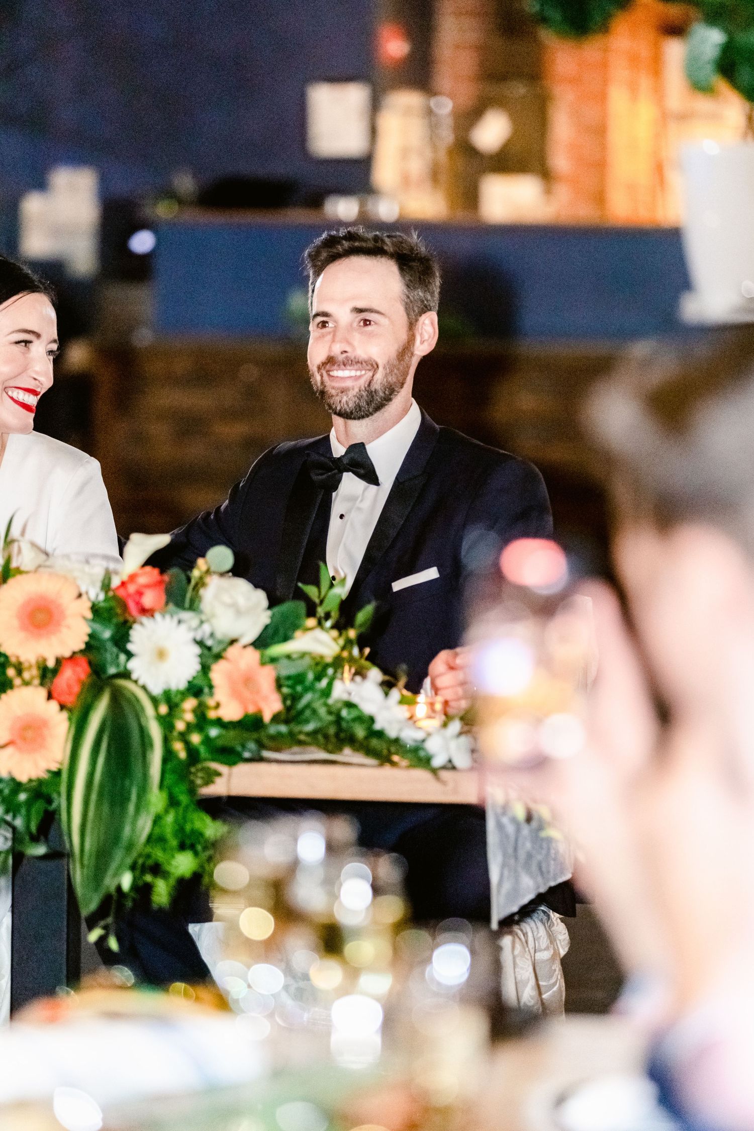Wedding guests enjoying conversation at an elegant reception with floral centerpieces and ambient lighting.