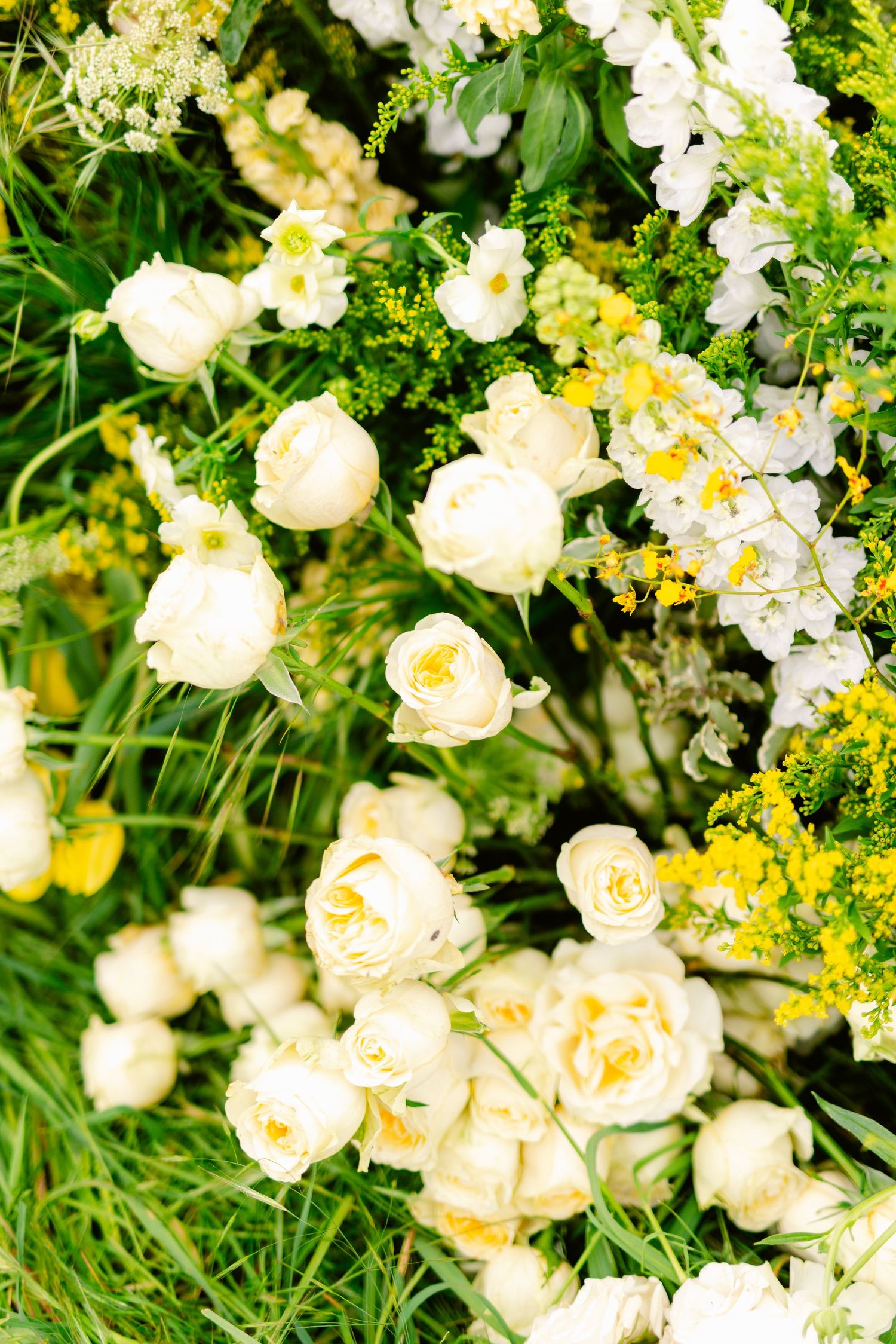 Delicate cream-colored roses and yellow wildflowers create a romantic garden arrangement against lush green foliage.