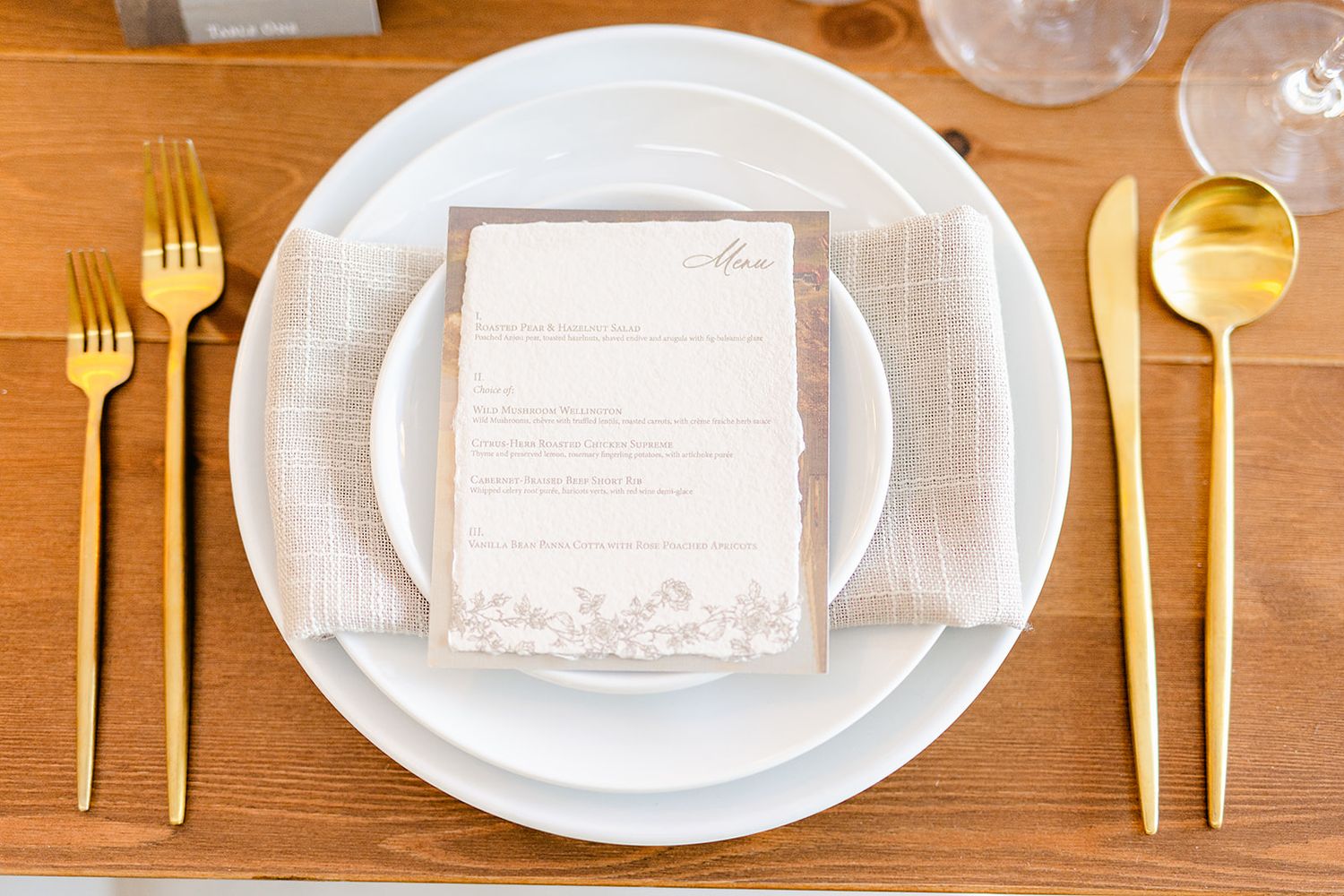 Place settings with gold flatware and white plates arranged on wooden tables for an elegant event.