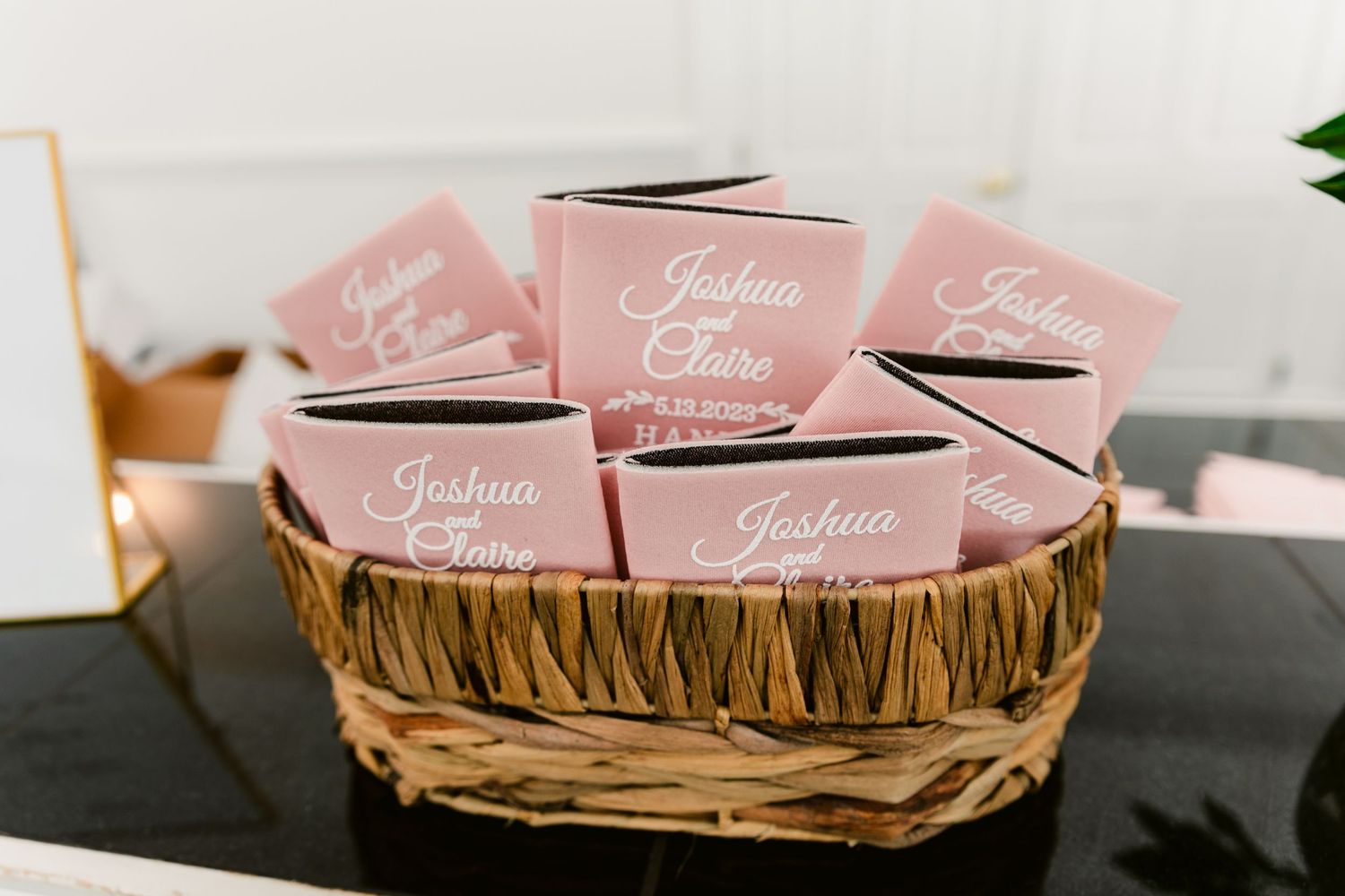 Pink wedding escort cards arranged in a rustic wooden basket with delicate calligraphy.