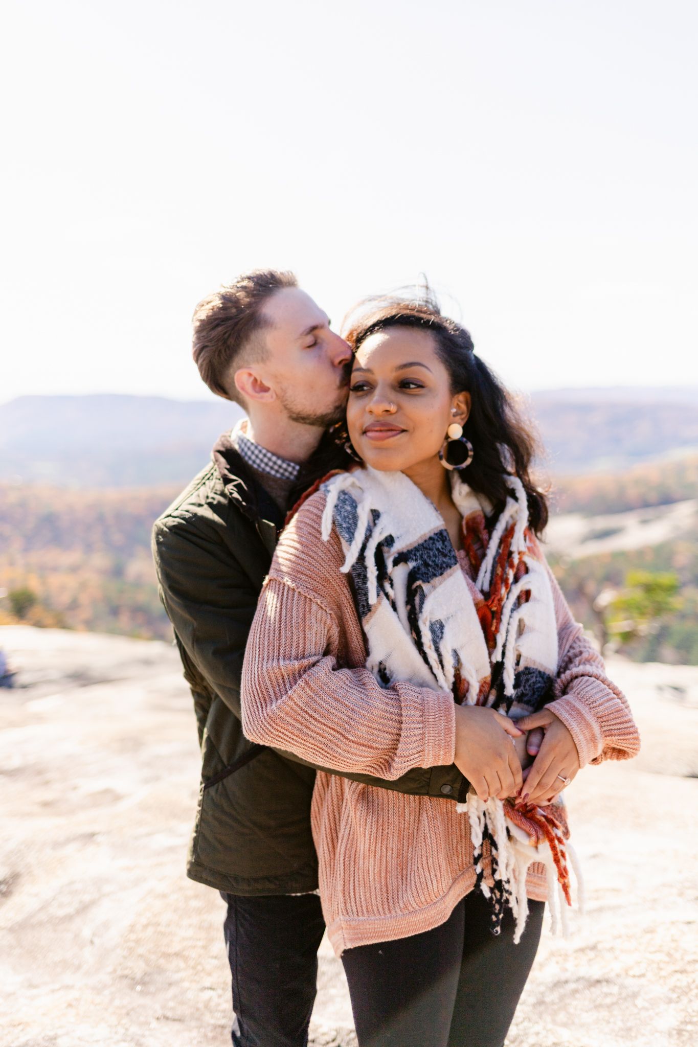 A couple embraces and shares tender moments while standing on a scenic overlook during an autumn day.
