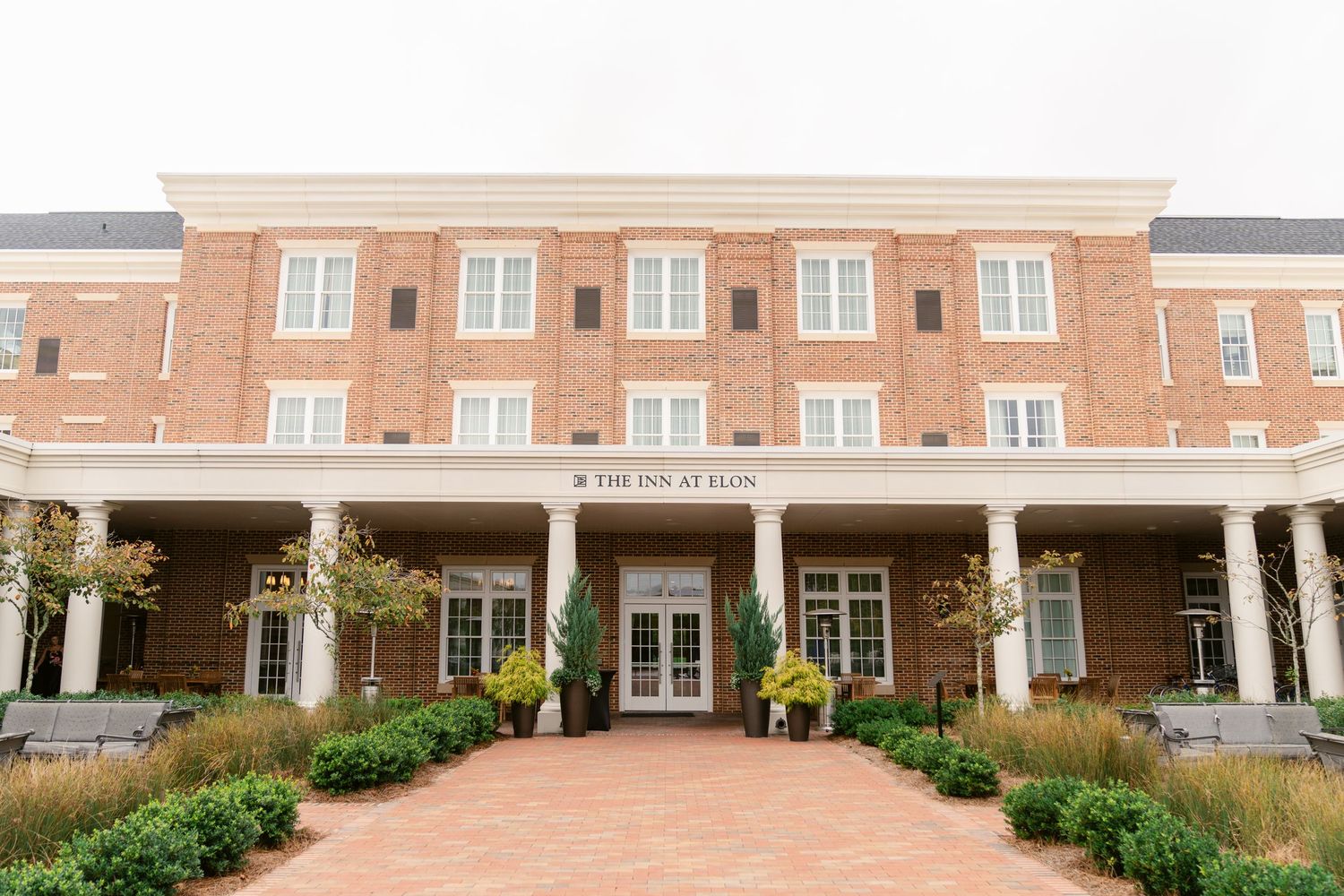 A series of connected brick buildings with white columns and landscaping form a modern senior living facility complex.