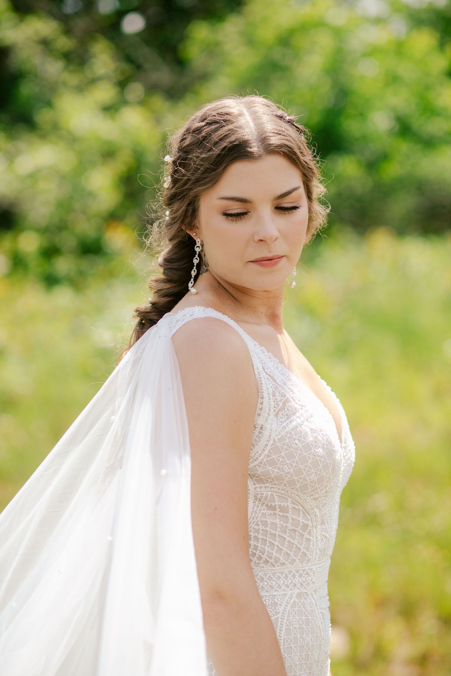 Dreamy outdoor bridal portrait featuring a detailed white gown and flowing veil against green foliage.
