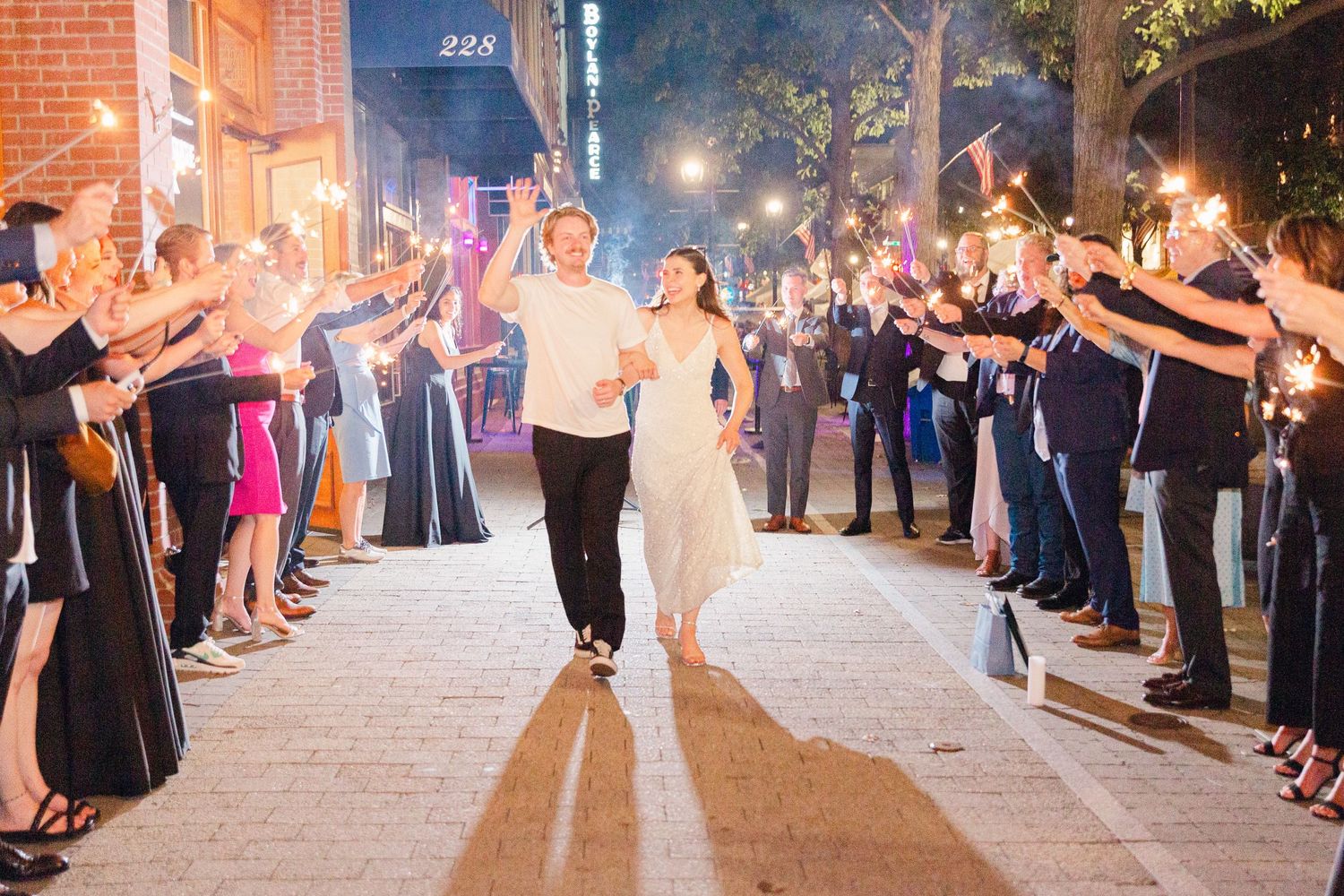 Newlyweds exit through a sparkler send-off with guests lining a brick pathway at night.