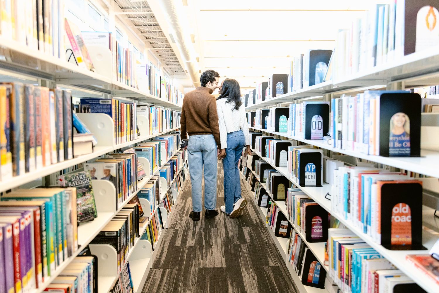 Long rows of library bookshelves extend into the distance under bright lighting.
